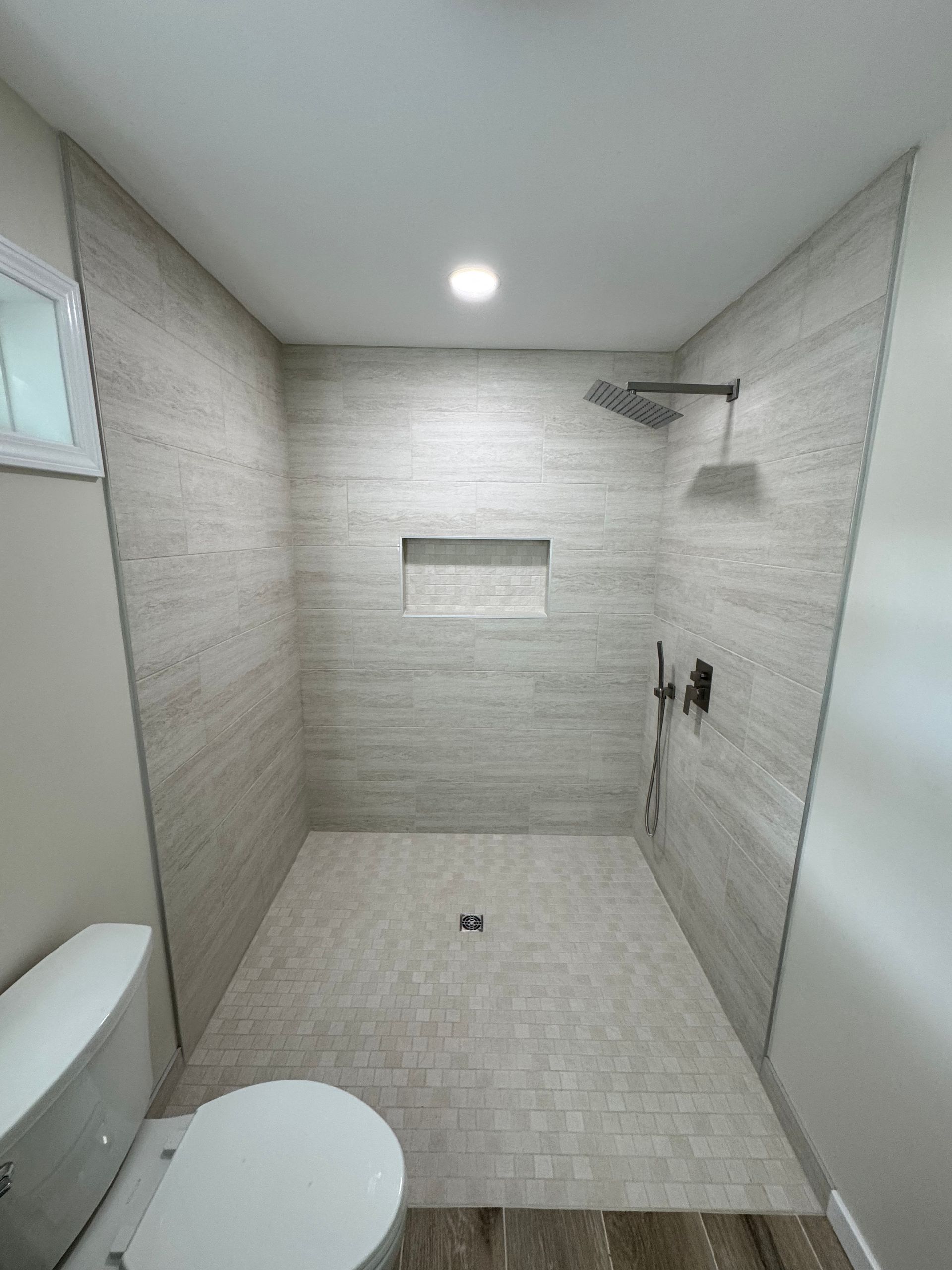 Small tiled bathroom with a walk-in shower, toilet, and recessed shelf under a ceiling light.