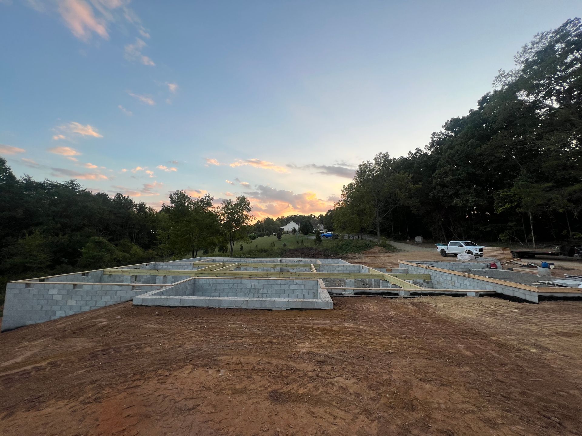 Graded lot with concrete foundation slabs at dusk, bordered by trees and a parked white truck.