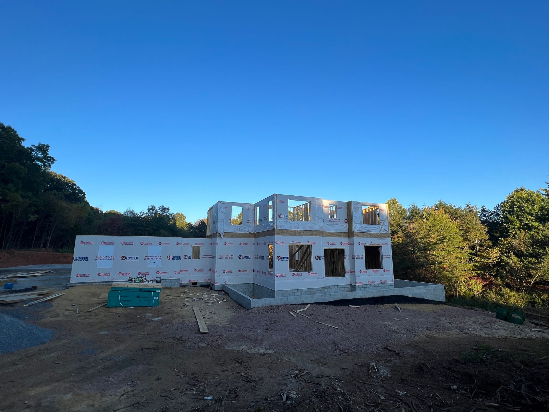 Partially built two-story white house on a dirt lot under a clear blue sky
