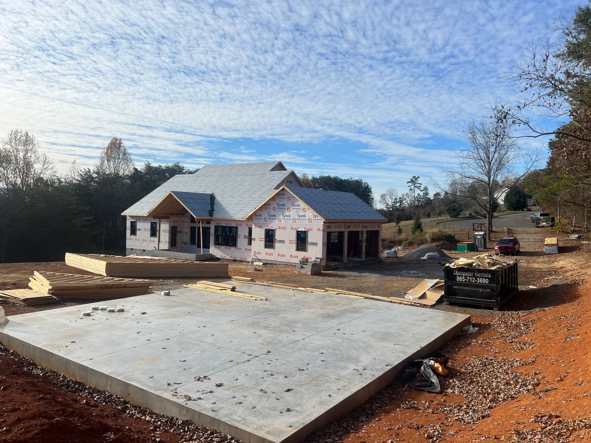 House under construction with concrete slab foundation, roof installed, and building materials around the site