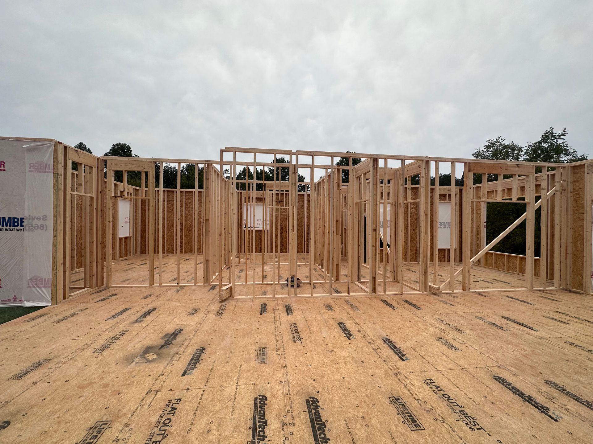 Wood-framed house under construction on a dirt foundation site beneath a cloudy sky