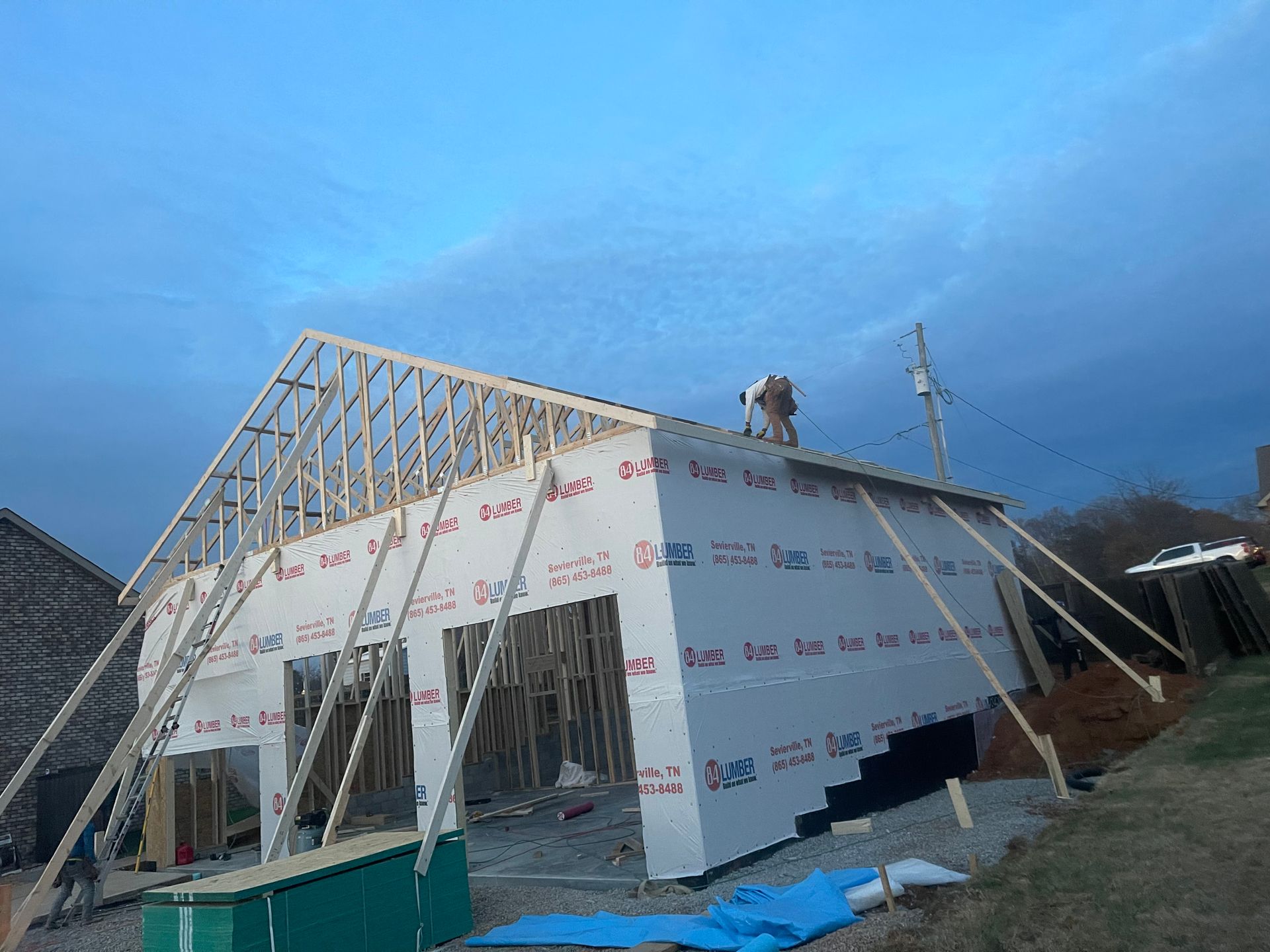 House under construction with concrete foundation and framing on a wooded lot under a blue sky