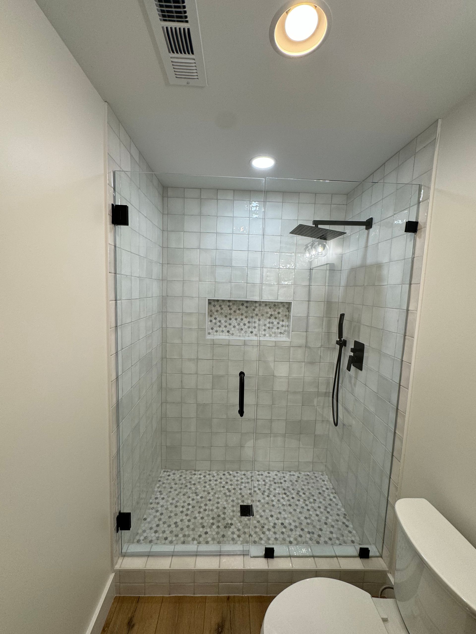 Modern walk-in shower with white tile, glass door, rainfall showerhead, and built-in bench.