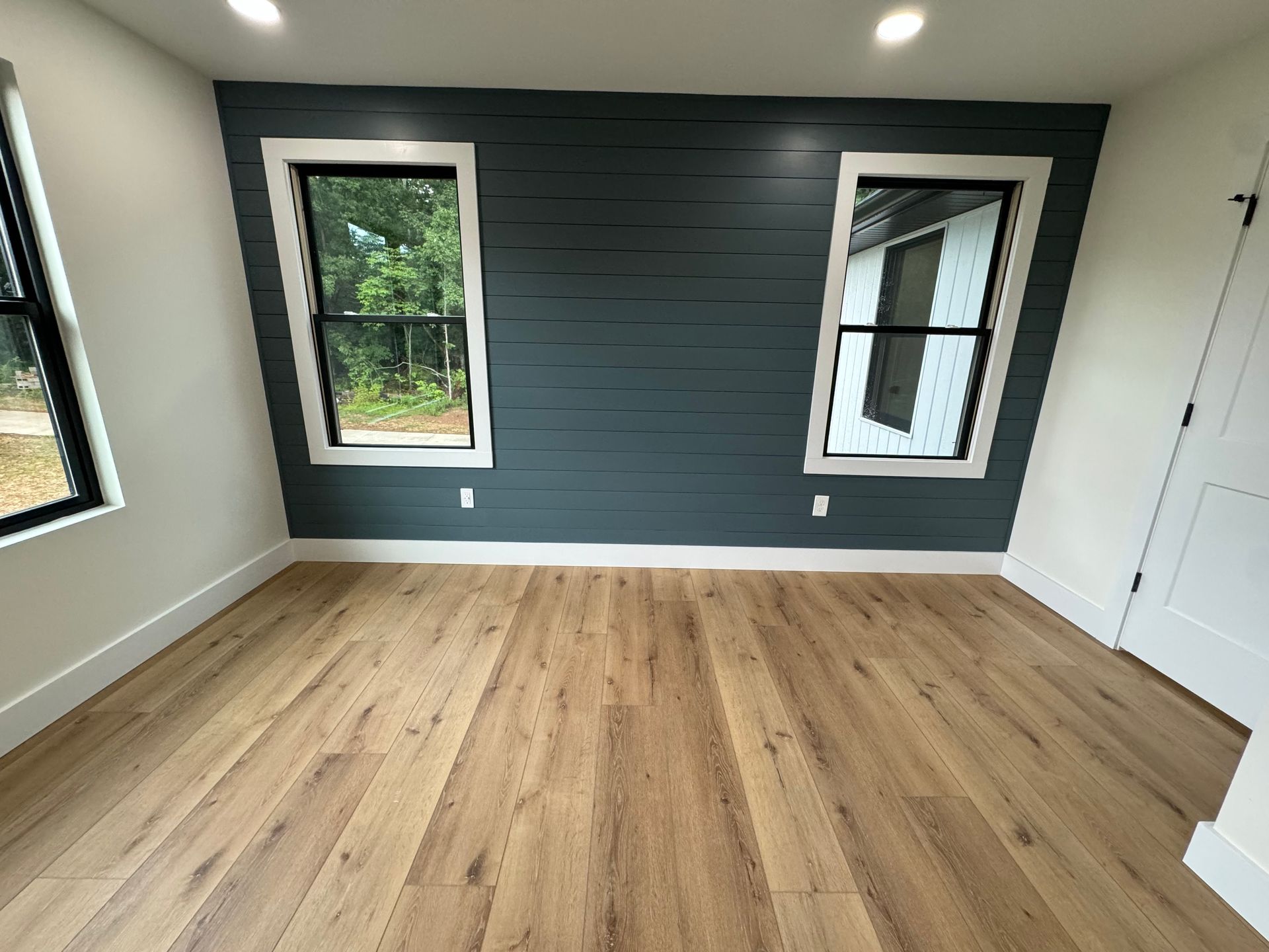 Empty room with wood floors, dark accent wall, and two windows
