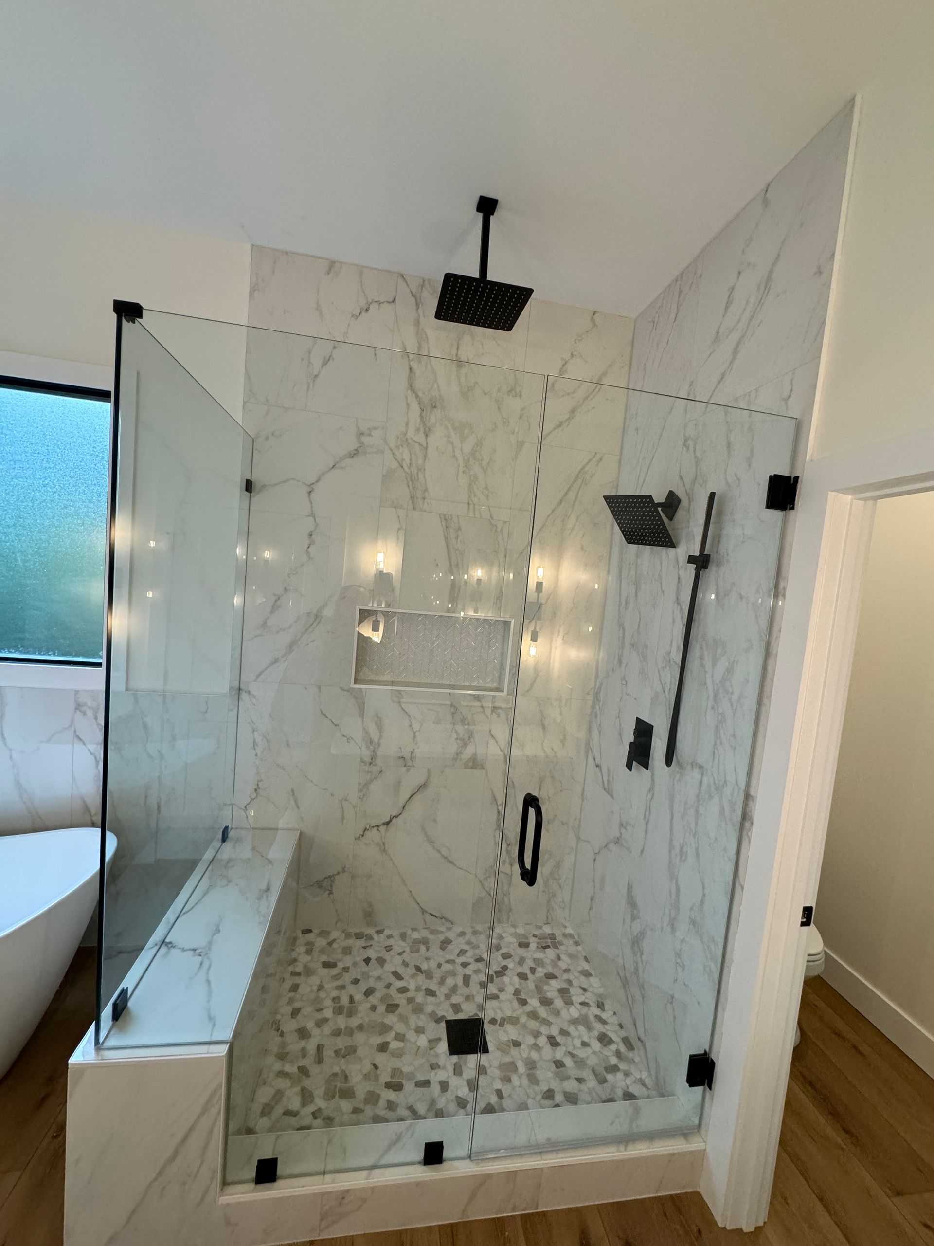 Glass walk-in shower with marble tile, black fixtures, and a rainfall showerhead