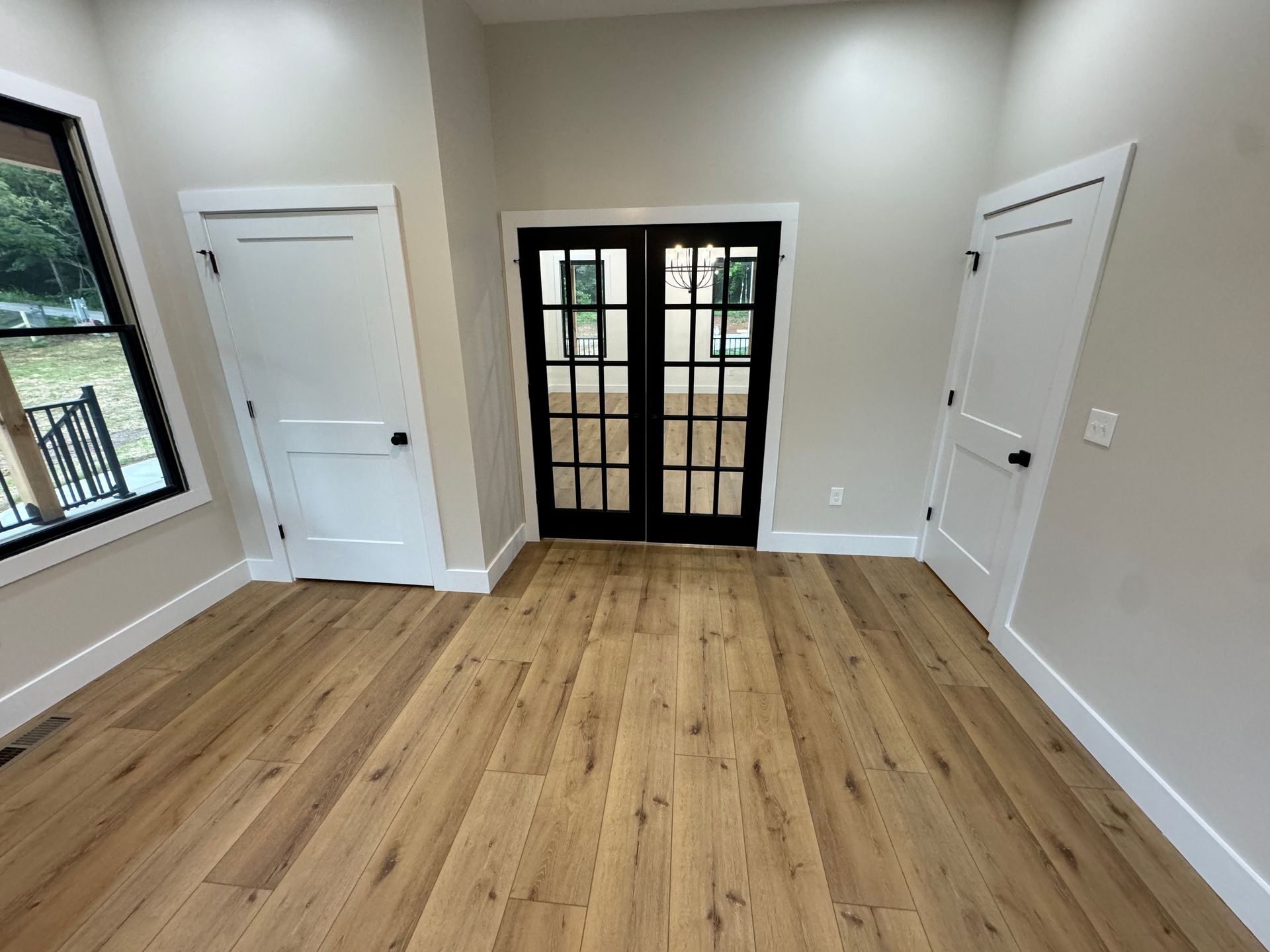 Empty room with light wood floors, white walls, and black French doors leading outside.