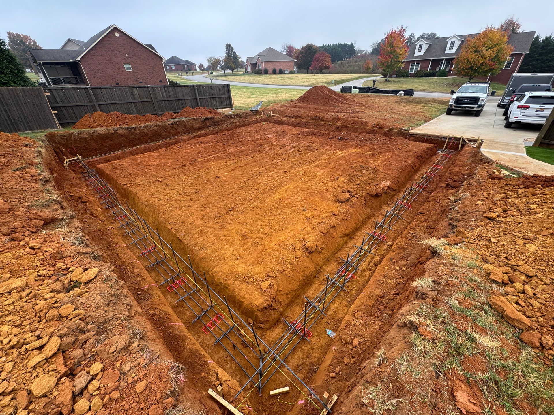 Large excavated dirt lot in a suburban neighborhood, with houses and parked cars nearby.