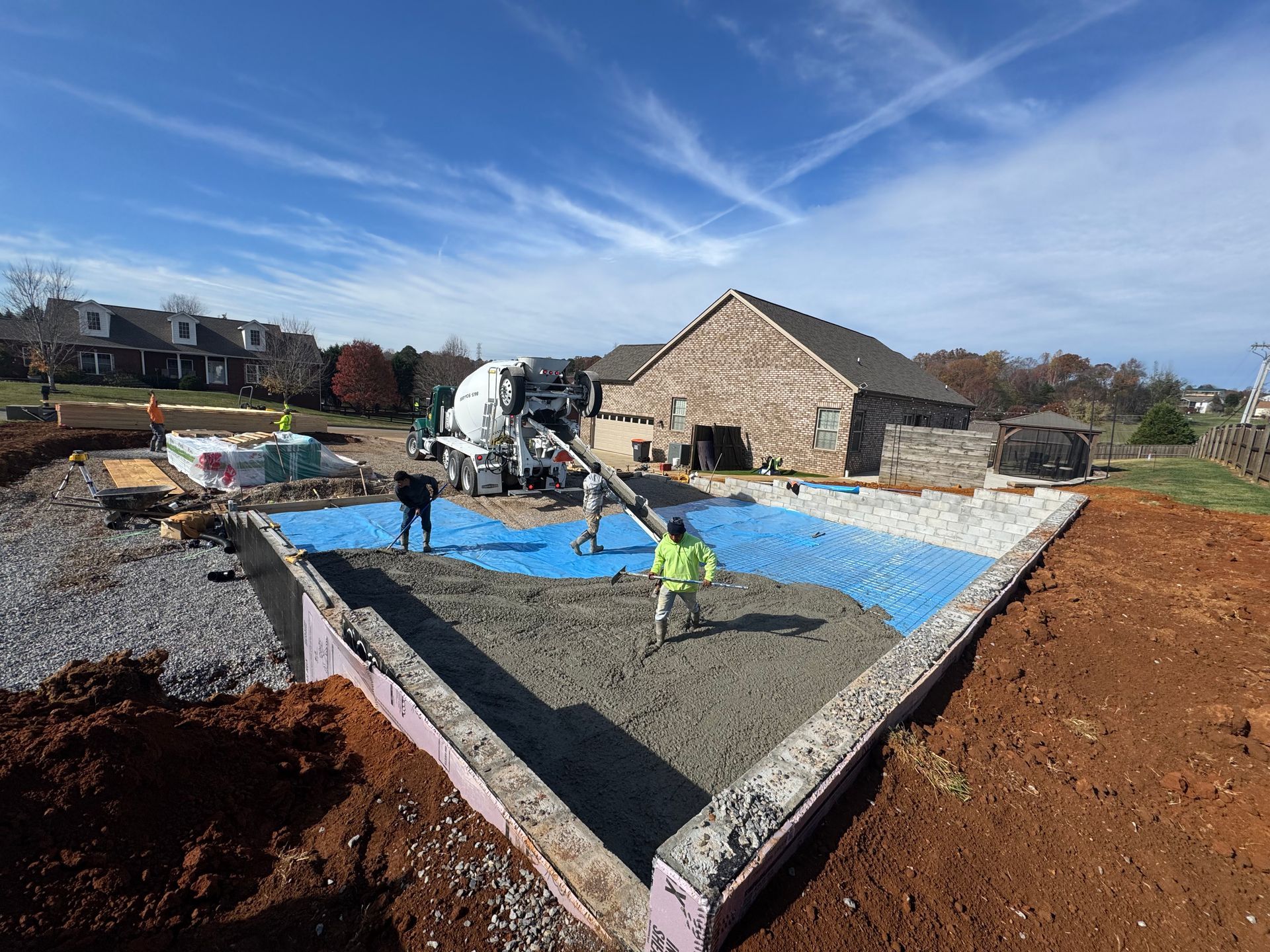 Workers pouring concrete for a house foundation on a construction site under a blue sky