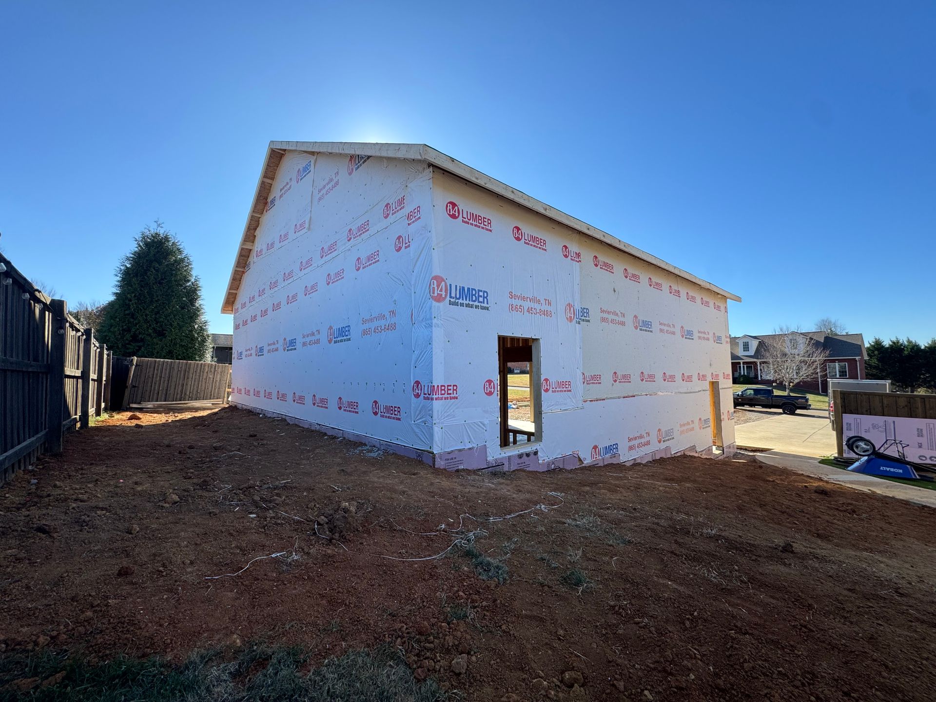 Partially built white house wrapped in house wrap on a dirt lot under a clear blue sky