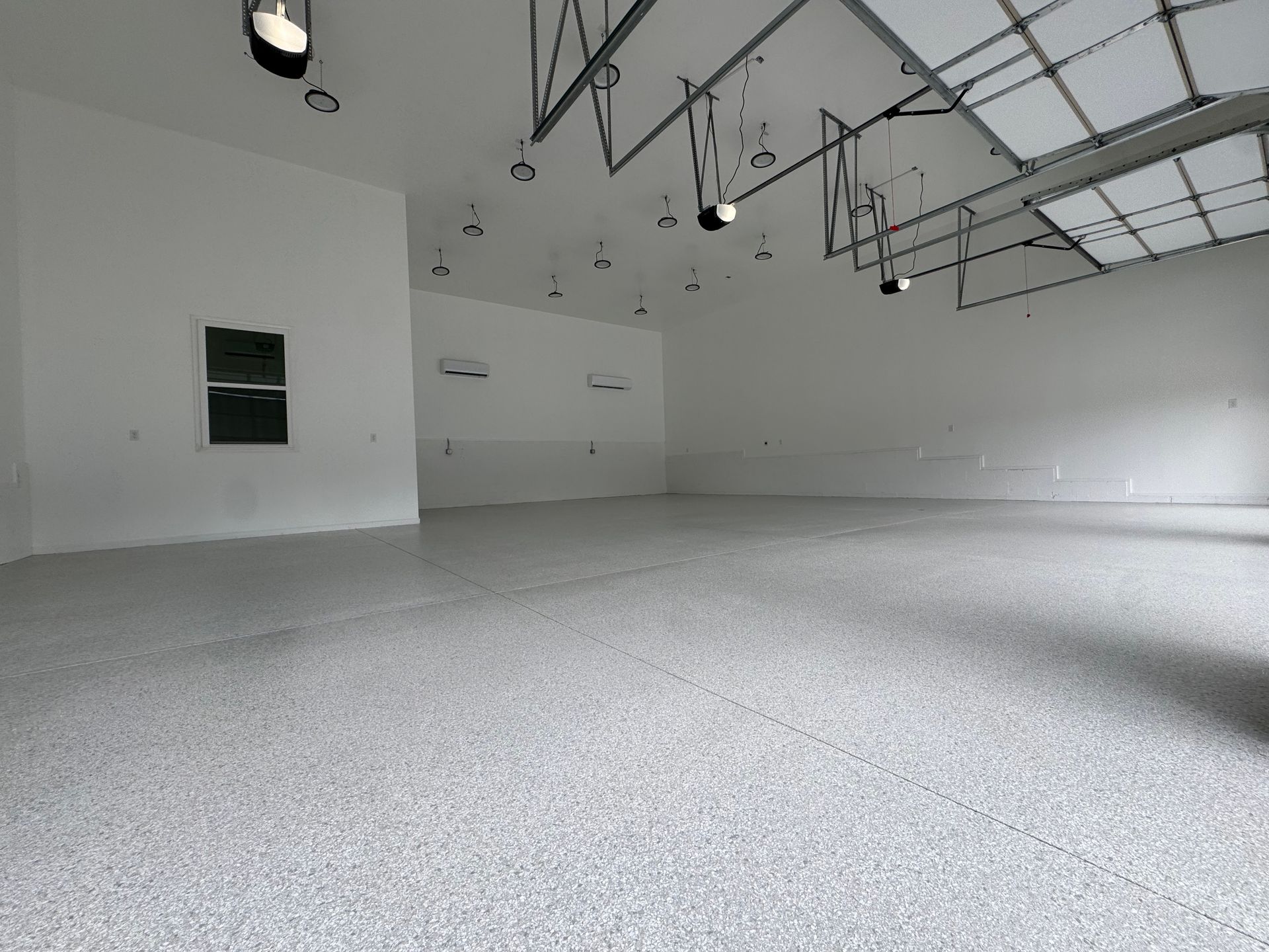 Empty white garage with a speckled floor and overhead lights, viewed from the side