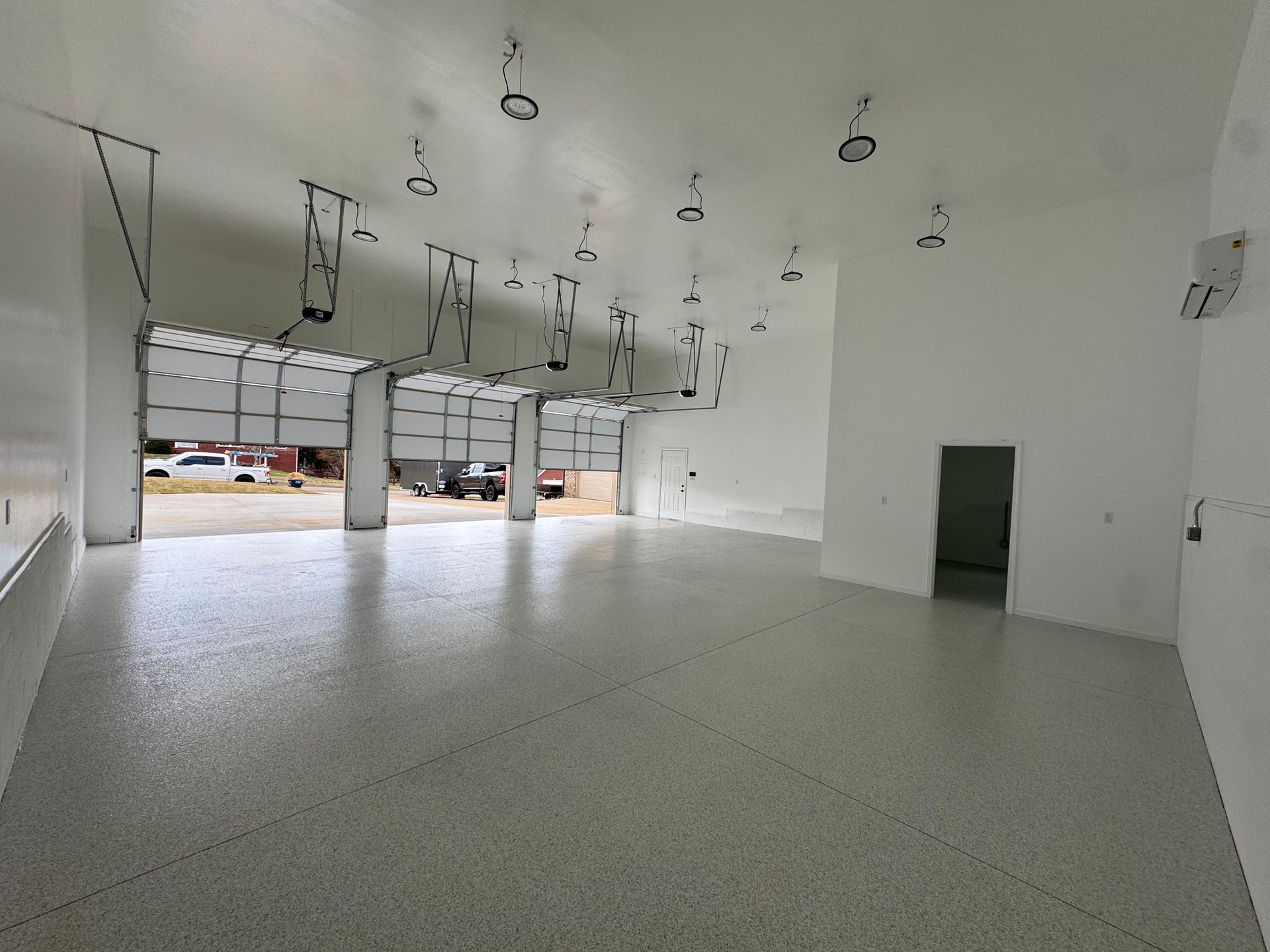 Empty white industrial showroom with high ceiling, large front windows, and a green door.
