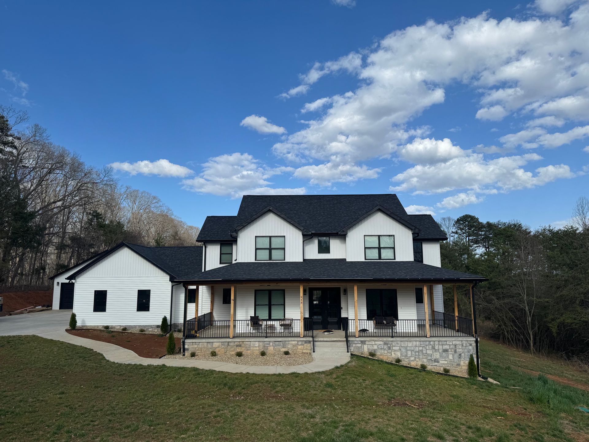 House under construction with crane, wrapped in white sheathing, surrounded by trees under a cloudy sky