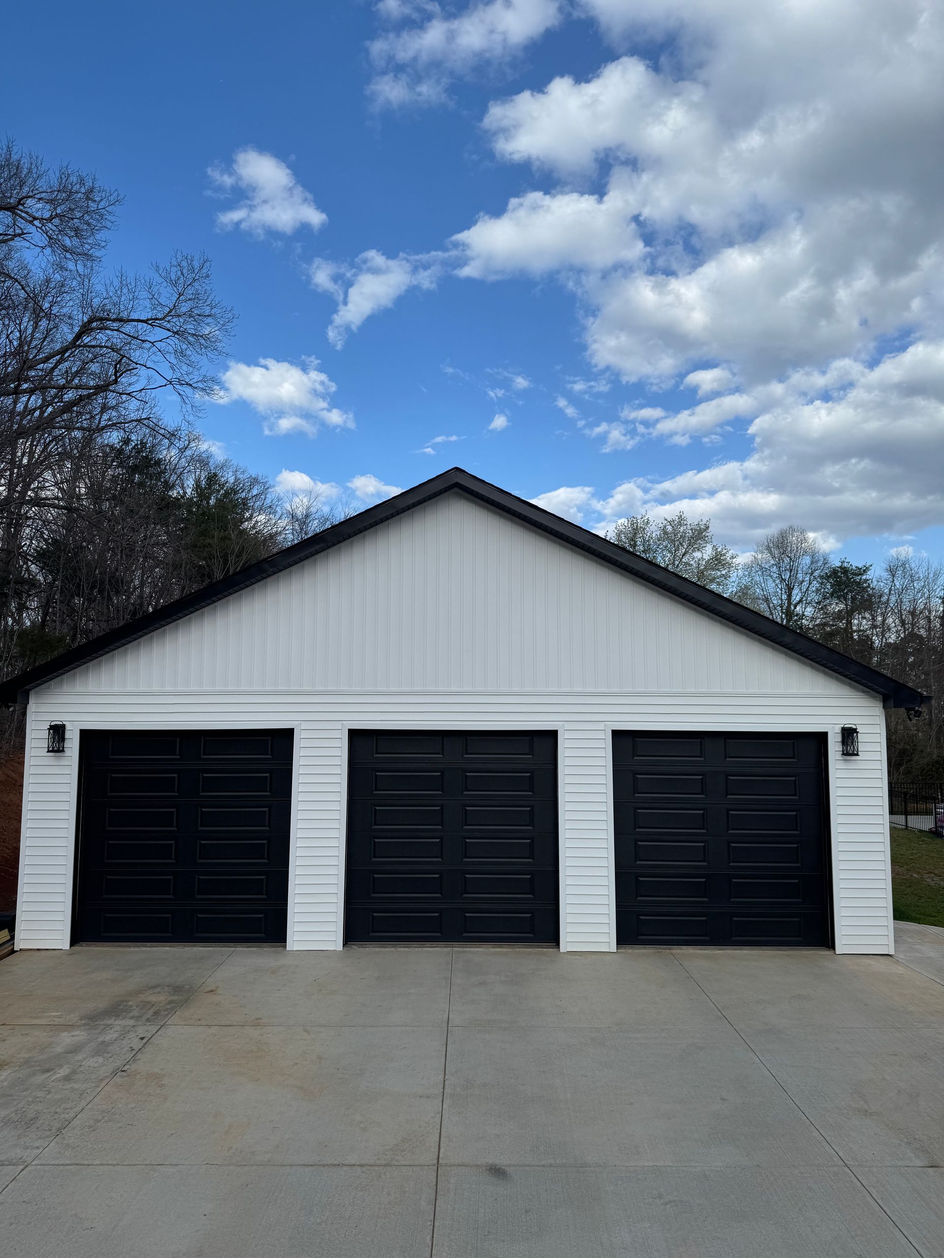 White three-car garage with black doors and a concrete driveway under a cloudy blue sky
