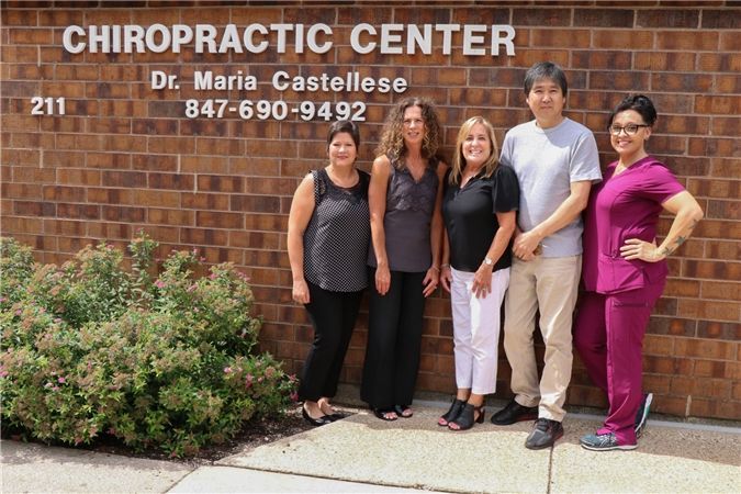 A group of five people stand in front of a chiropractic center. The brick building has a sign with the name of the center and the doctor's name.
