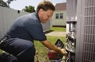 Man kneels beside an outdoor HVAC unit, inspecting wiring with tools in a yard.