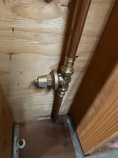 Copper pipes and a brass valve attached to wooden framing. The valve has a small, brass-colored dial.