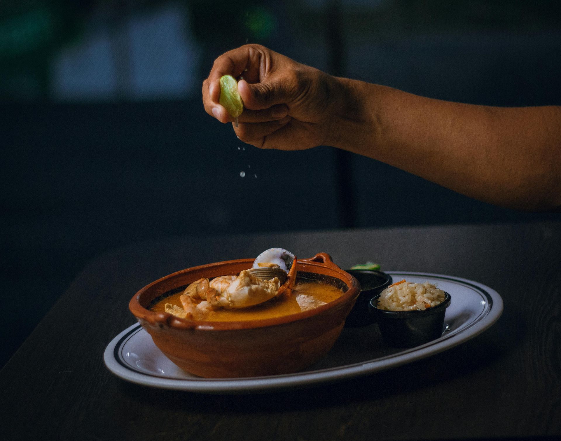 A person is holding a lime over a bowl of soup.