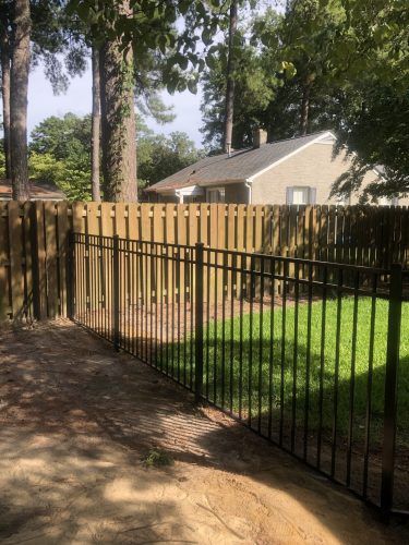 A wooden fence with a metal fence in front of a house.