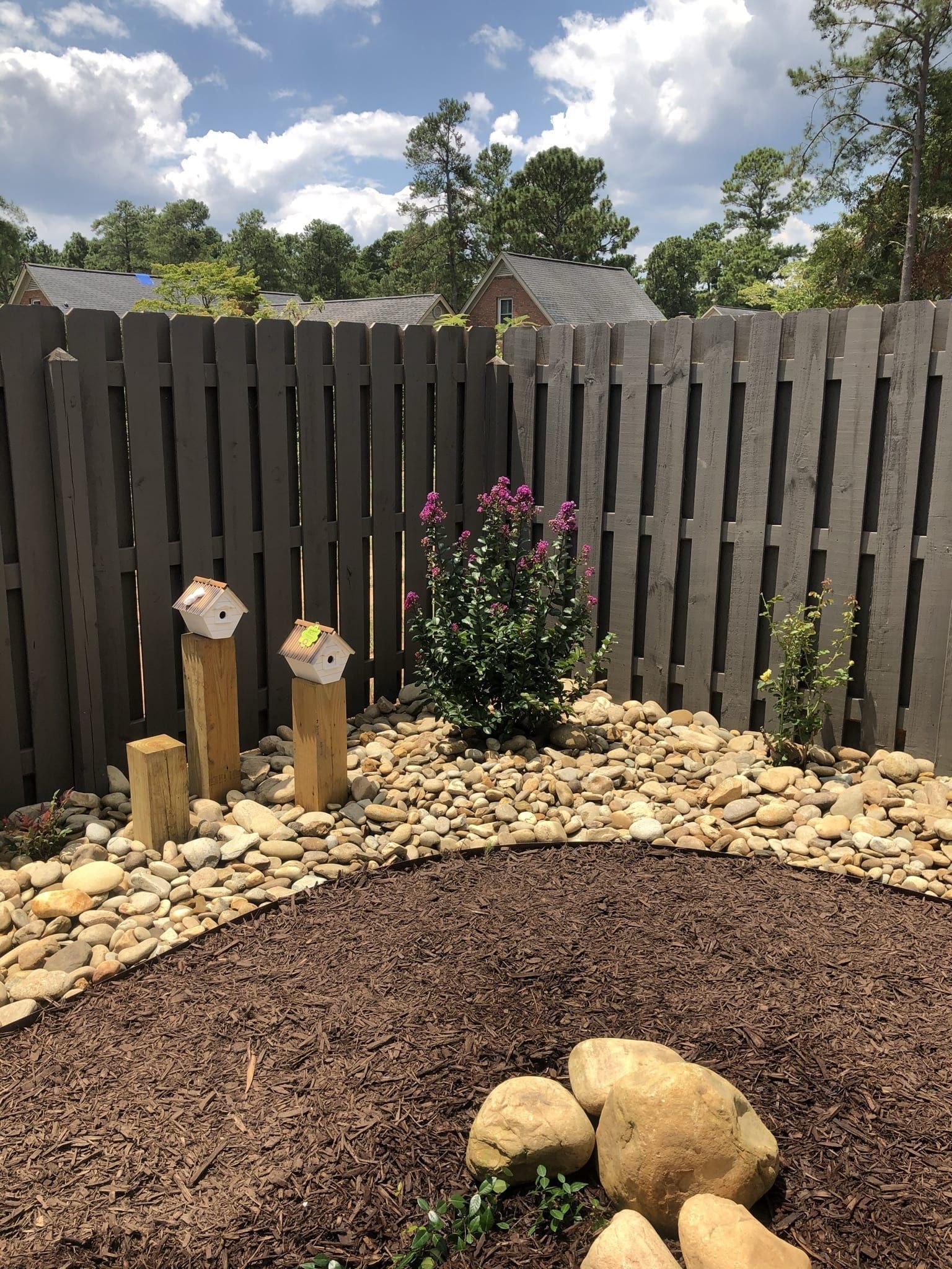 A wooden fence is surrounded by rocks and flowers in a garden.