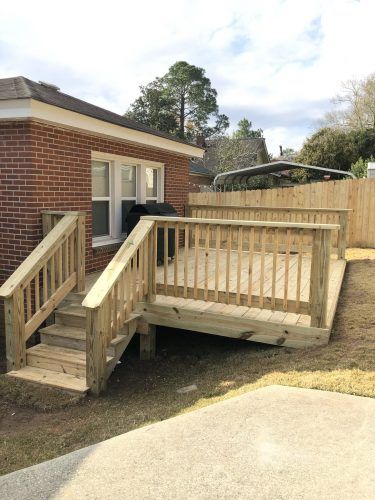 A wooden deck with stairs is in front of a brick house.