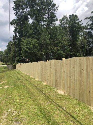 A wooden fence surrounds a grassy field with trees in the background.