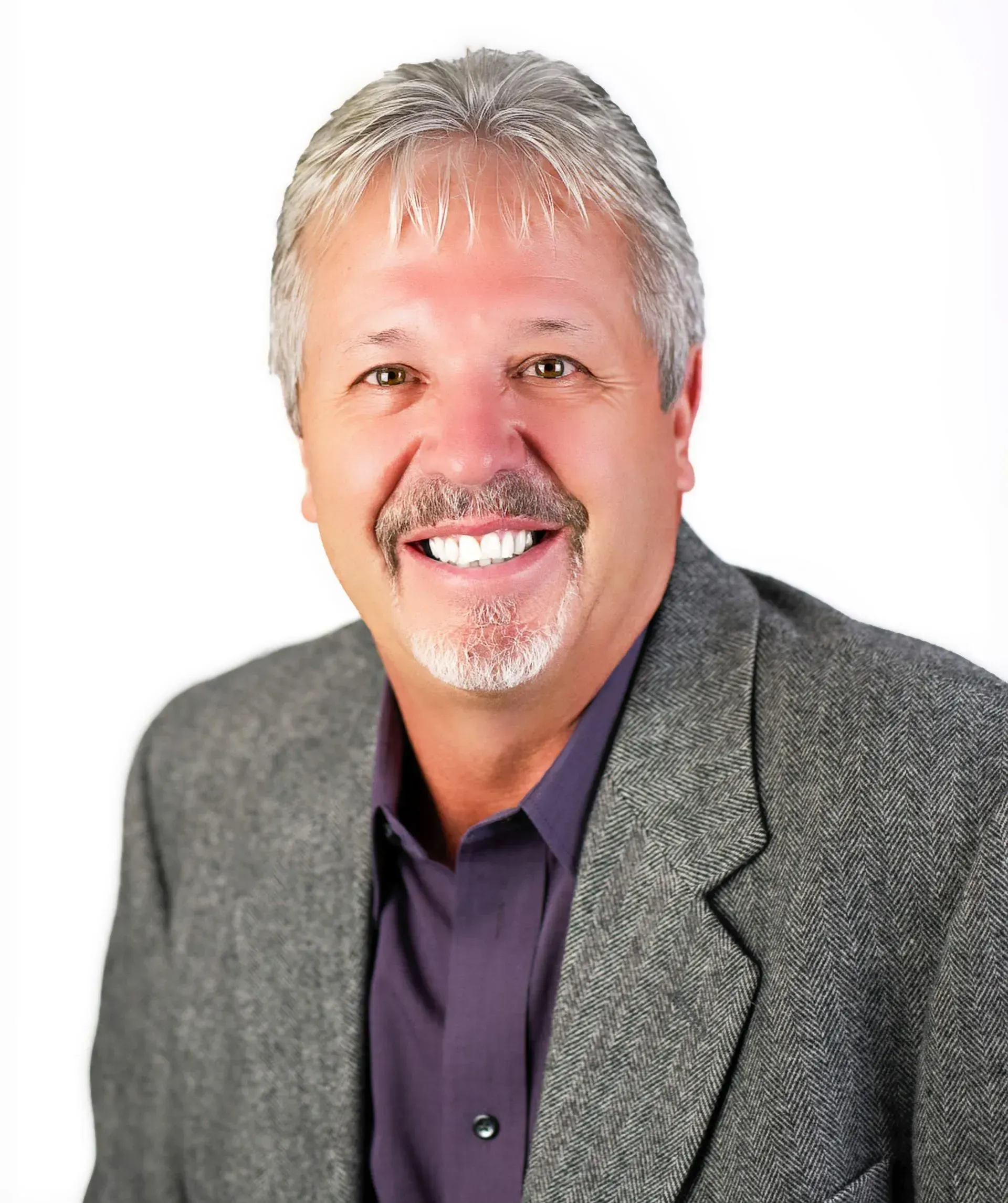 A person with short, light-brown hair and a mustache smiling in a purple button-down shirt and a grey textured blazer.