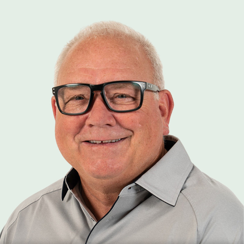 Man with glasses smiling, wearing a gray shirt, against a light green background.