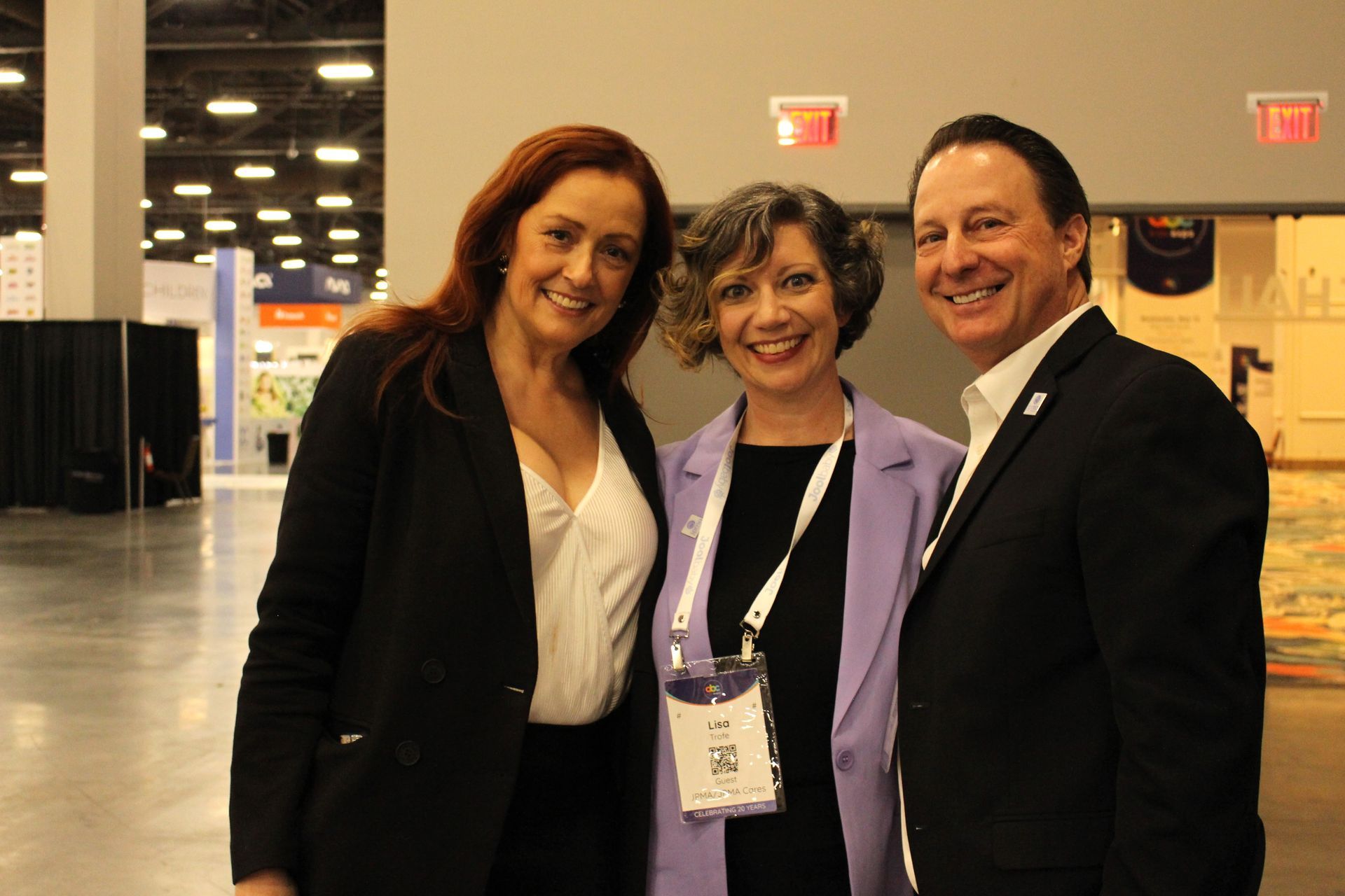 Three people smiling, posing for a photo at a convention. 