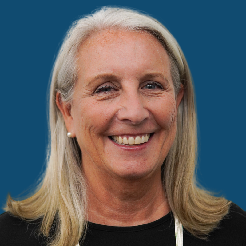 Woman with blonde hair smiling, wearing a black top against a blue background.
