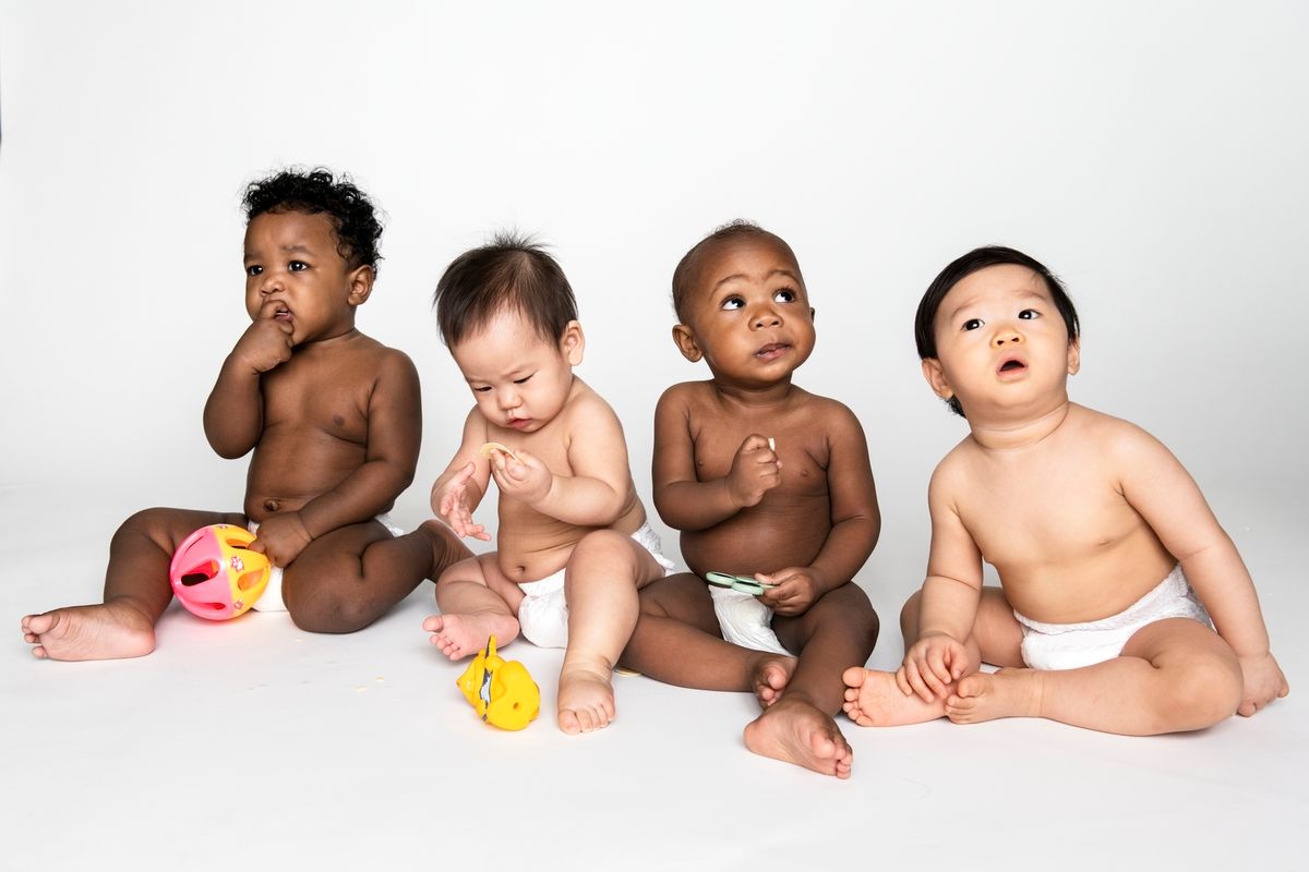 Four babies sitting together, looking upward. They are different skin tones and wearing diapers.