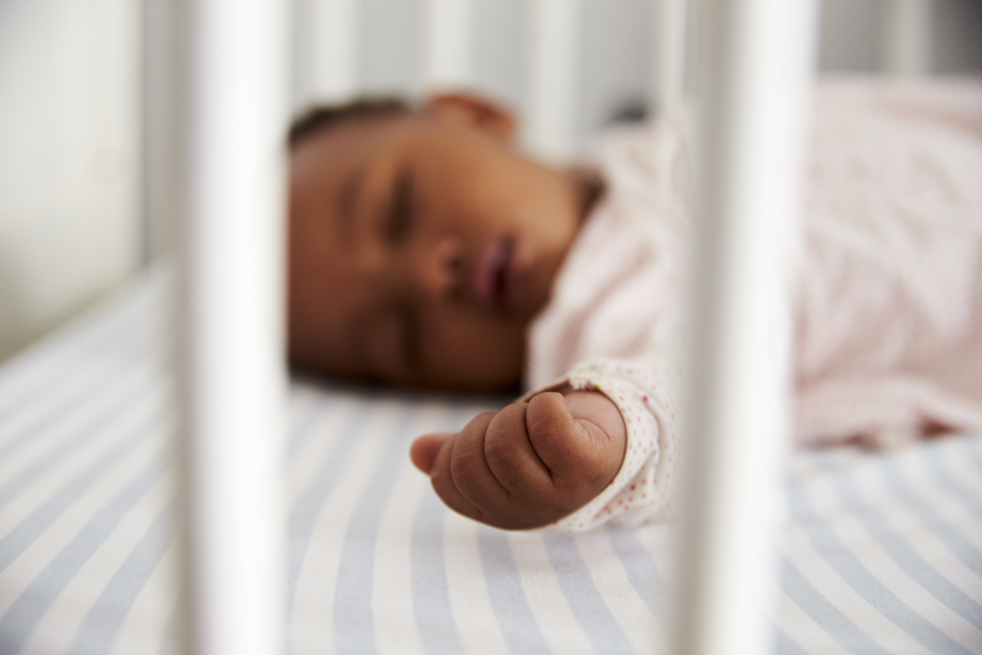 Sleeping baby in a crib, arm extended, soft focus. Represents safe sleep environment.