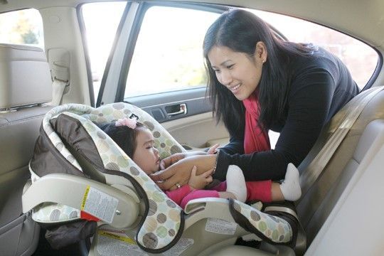 Woman securing child in car seat. Beige and pink colors. Sunlight.