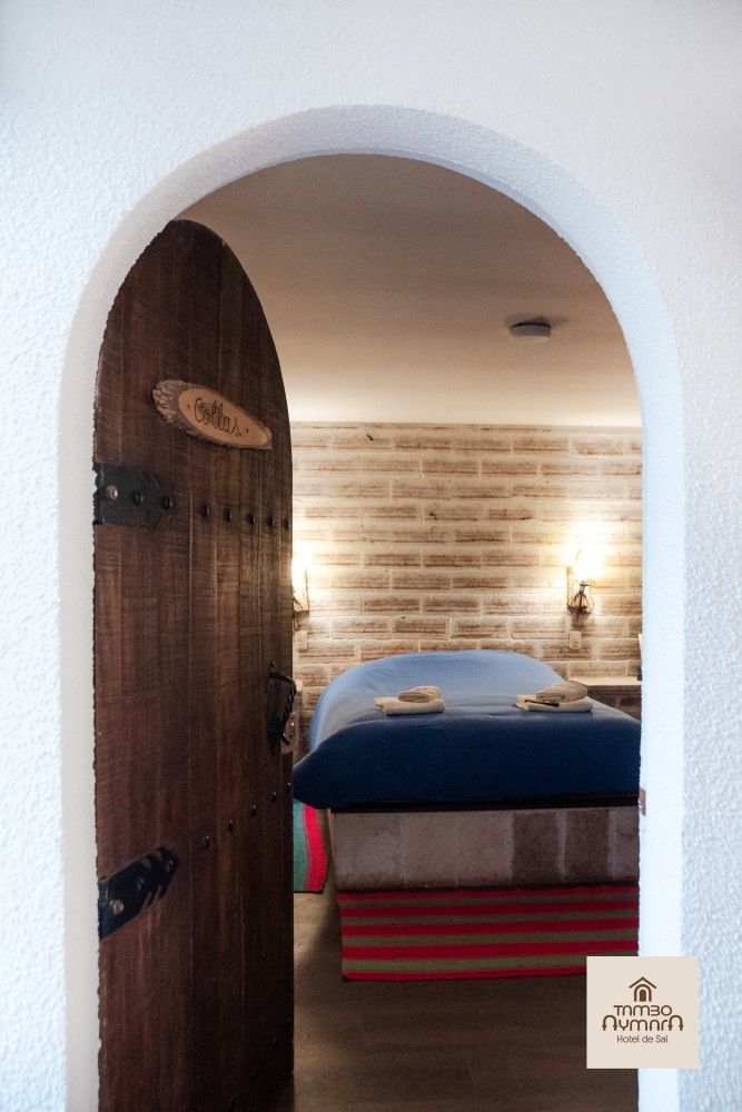 Una puerta arqueada da paso a un acogedor dormitorio con una cama azul, una pared decorativa de ladrillo .