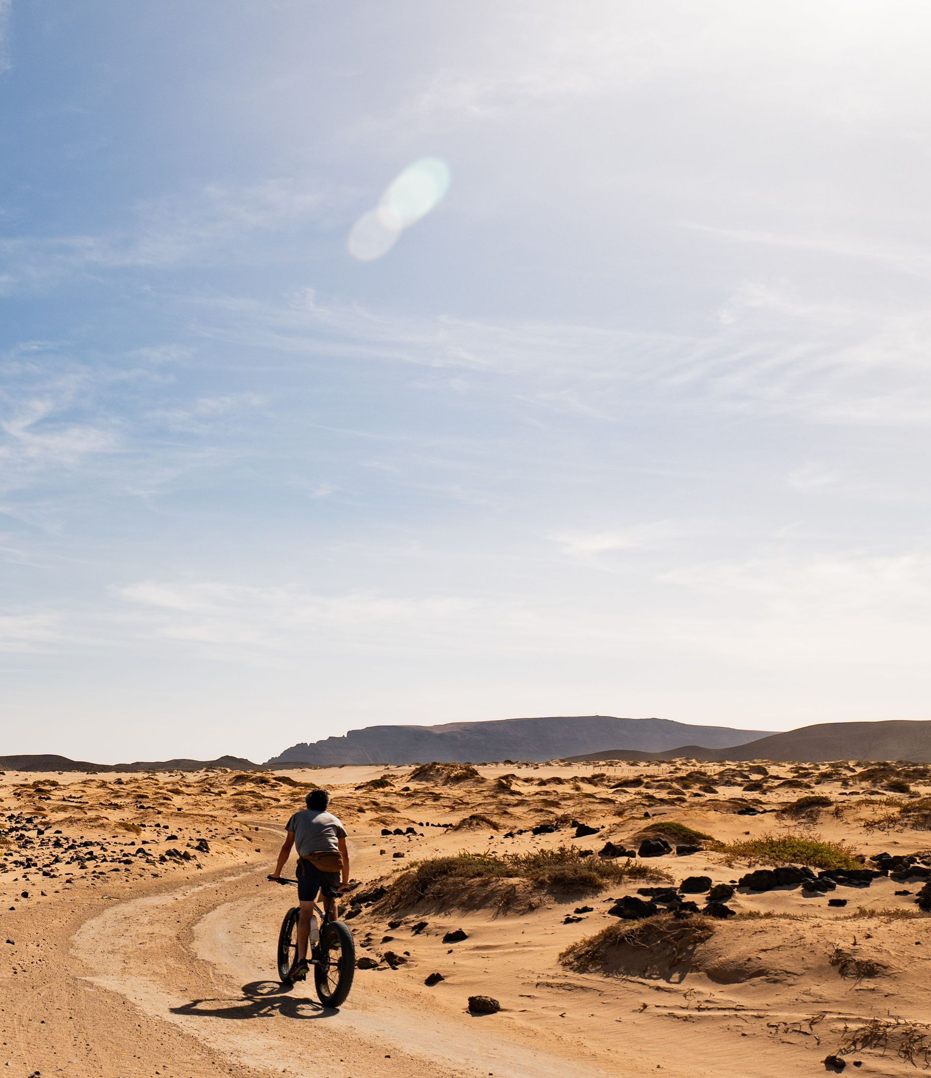 Ciclista recorriendo un sendero arenoso en el desierto bajo un cielo azul brillante.