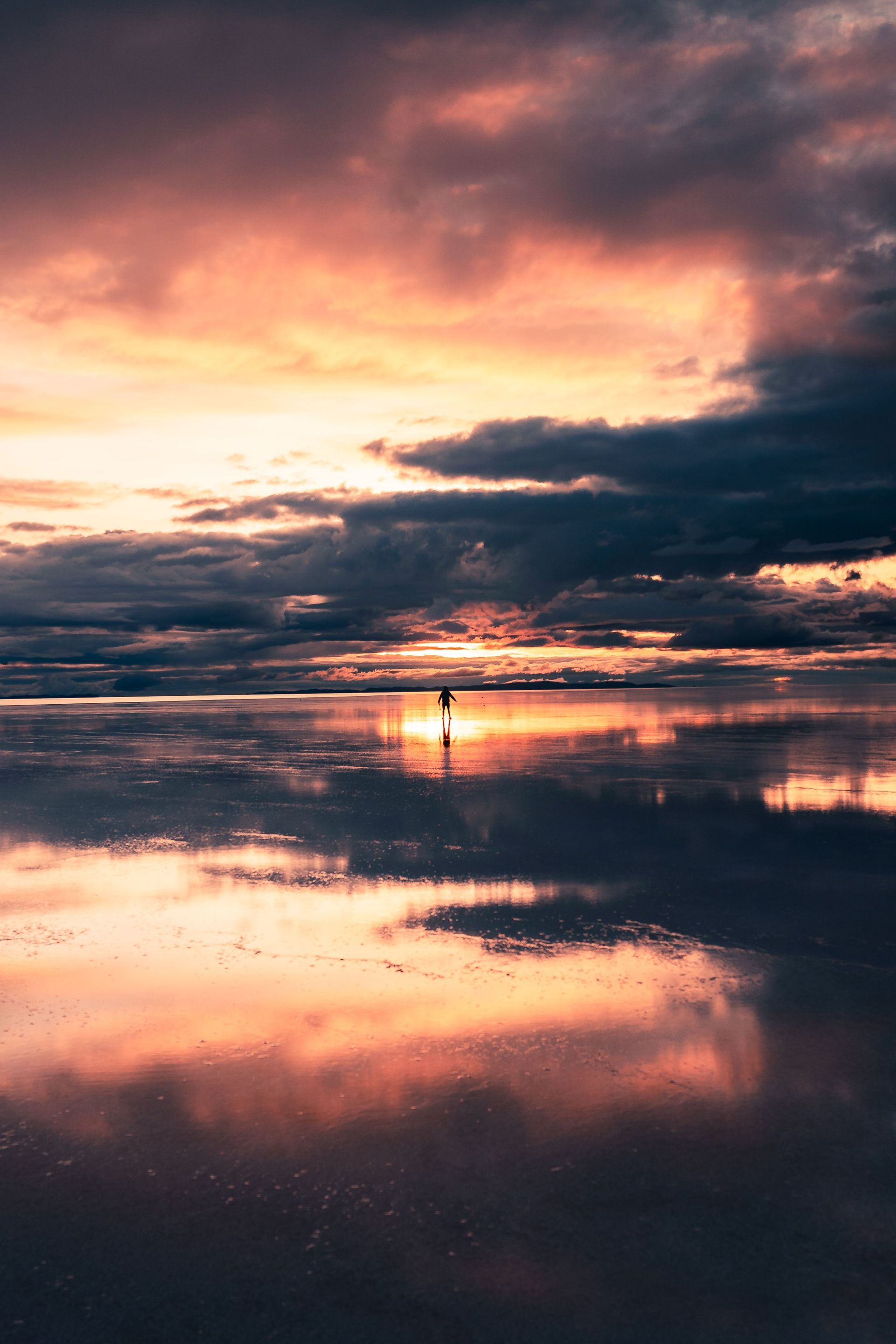 Puesta de sol sobre una tranquila costa reflectante con nubes espectaculares y un cálido cielo naranja rosado.
