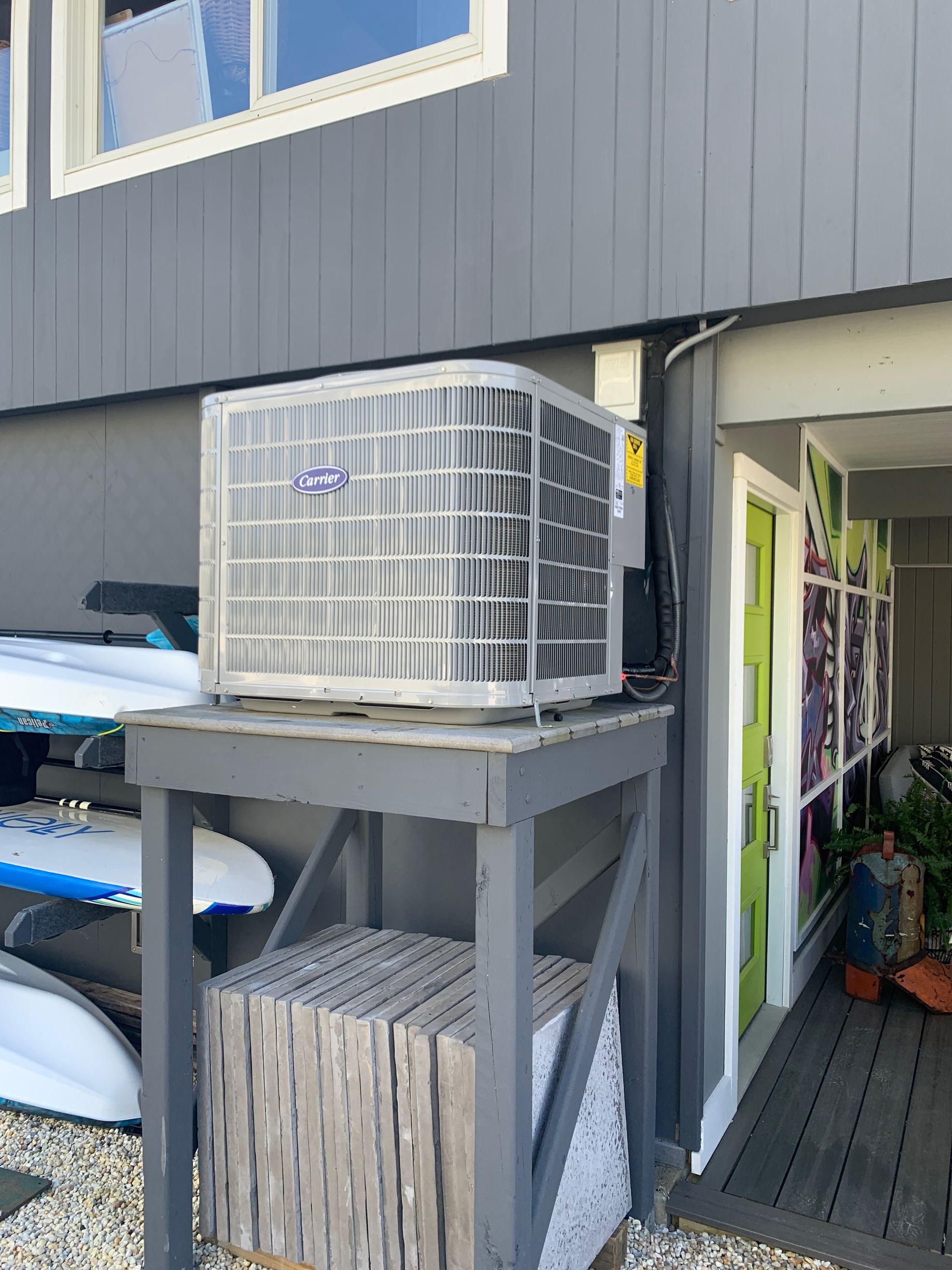 Outdoor air conditioner unit on a gray stand beside a dark gray building entrance.