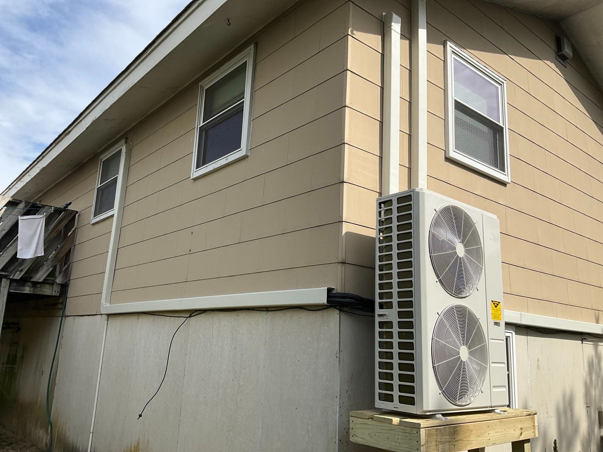 Two-story beige house exterior with wall-mounted air conditioner units and visible siding panels