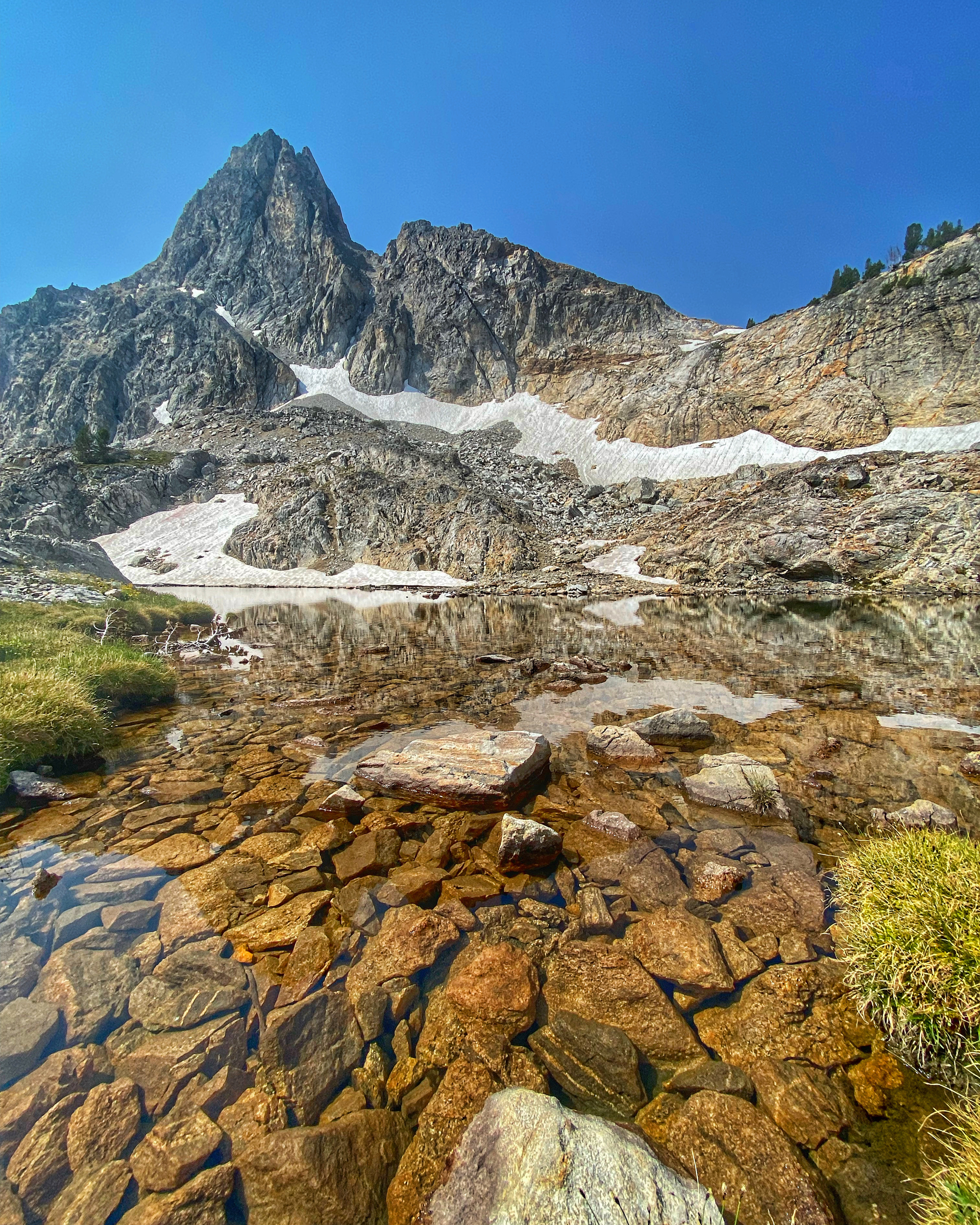 Rocky mountain peak reflected in clear water, blue sky above.