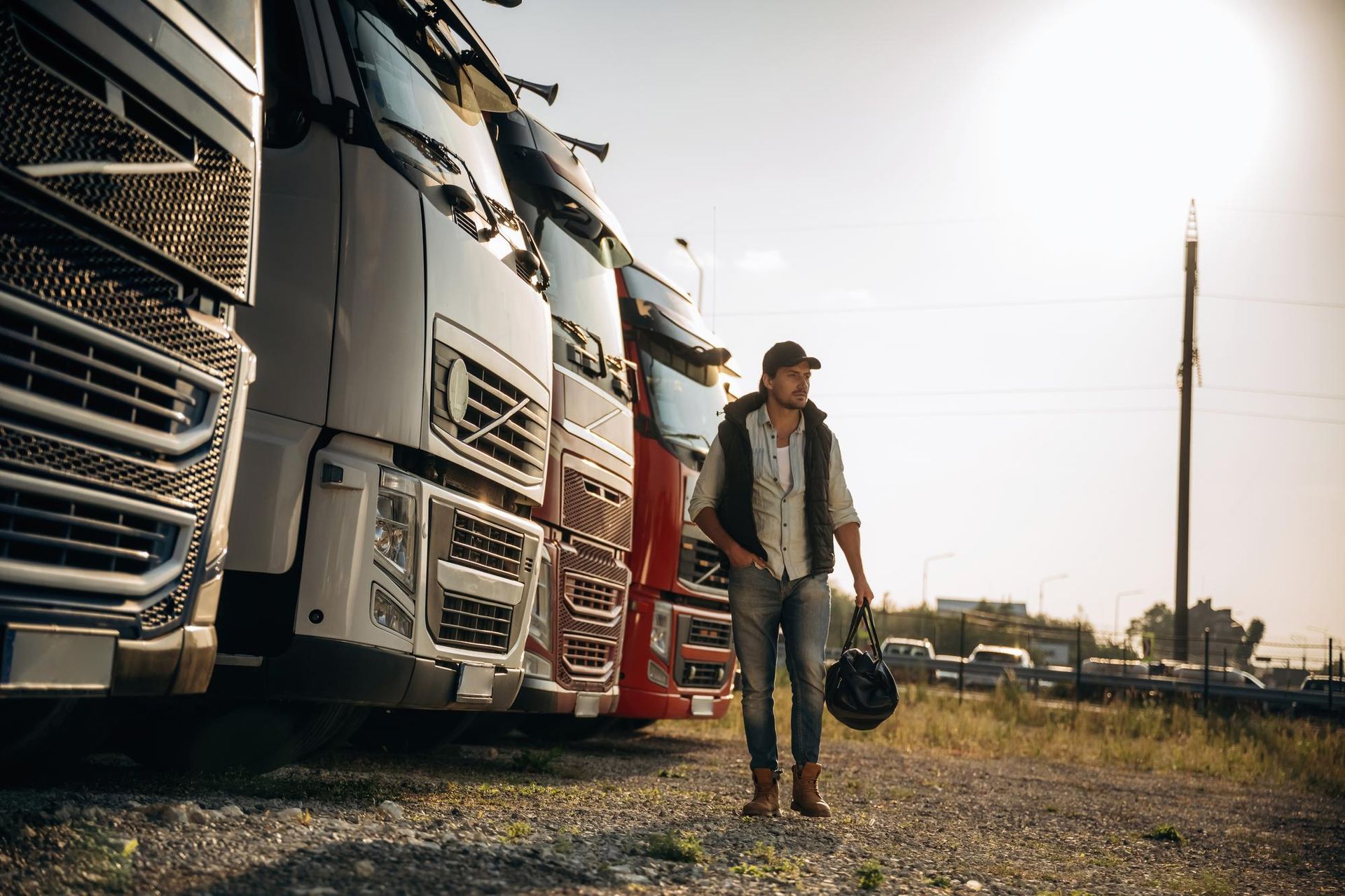 Man walking between parked semi trucks on a gravel lot at sunset