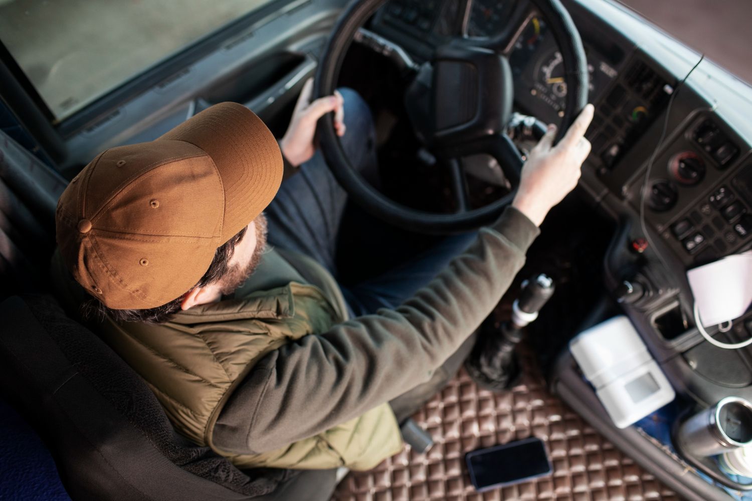 Person in a brown cap driving a vehicle, seen from above inside the cab.
