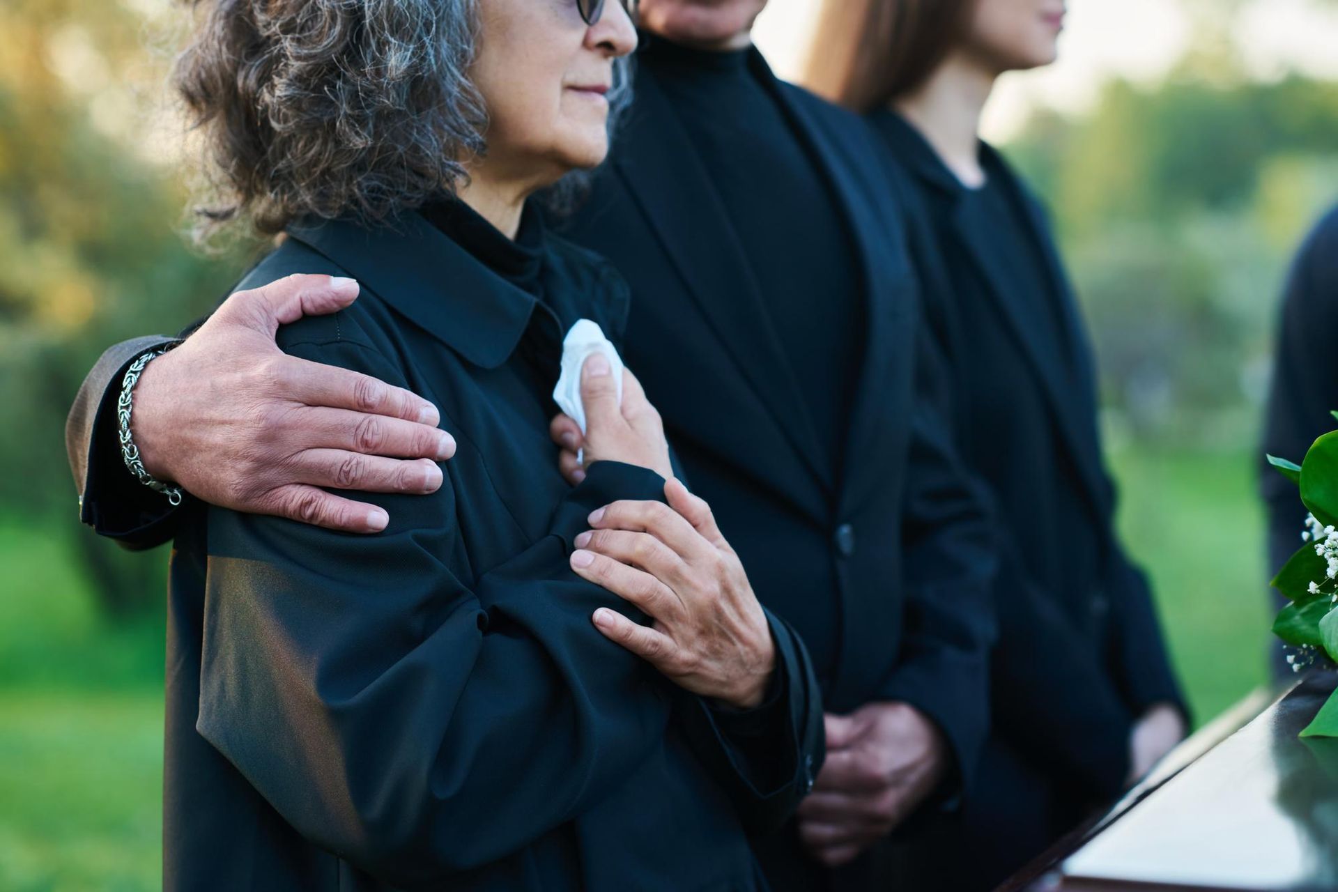 Two people in black clothing standing close together at an outdoor memorial service