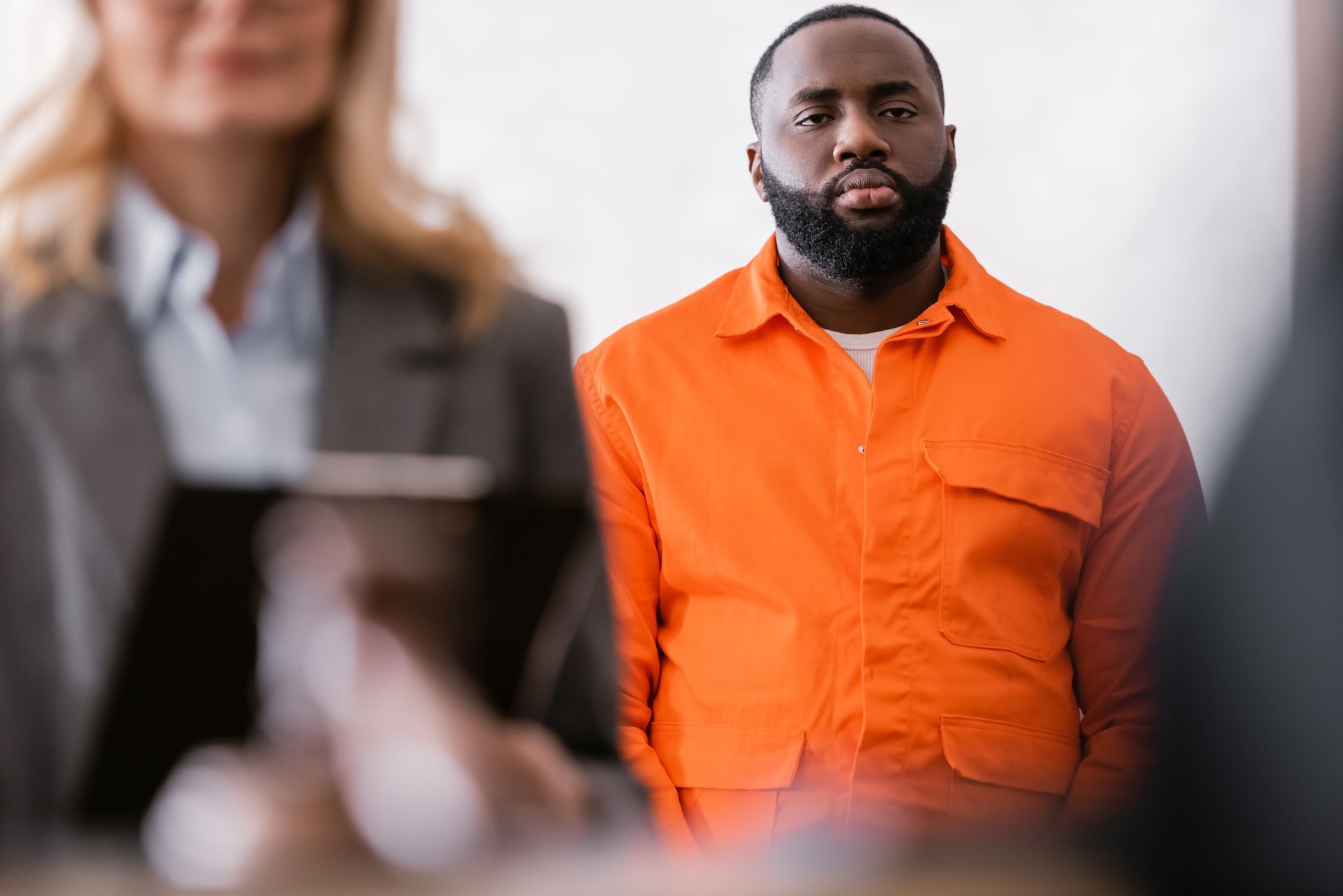 Man in orange shirt standing in a blurred office setting, looking forward