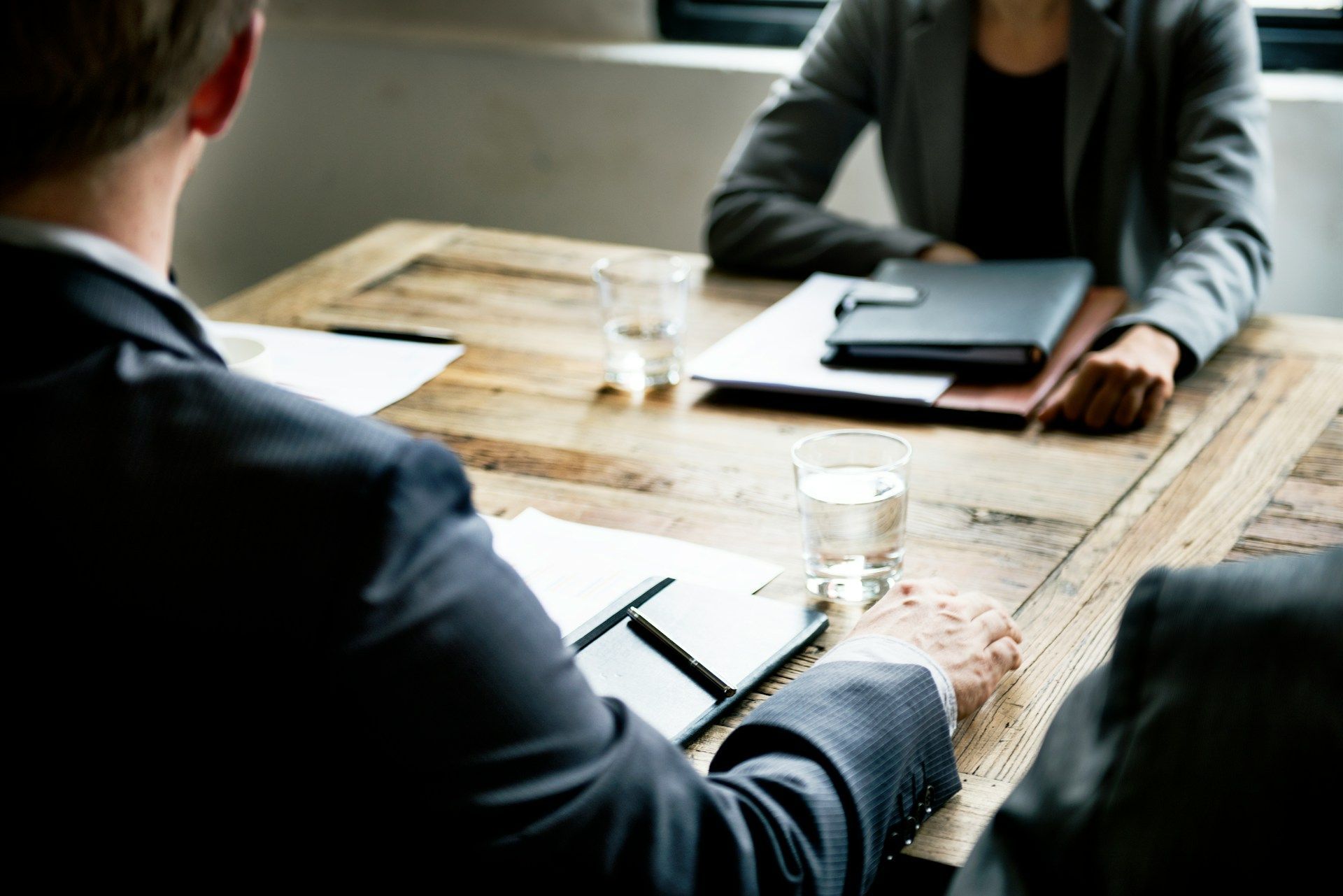 Business meeting at a wooden table with notebooks, coffee glasses, and two people seated across from each other