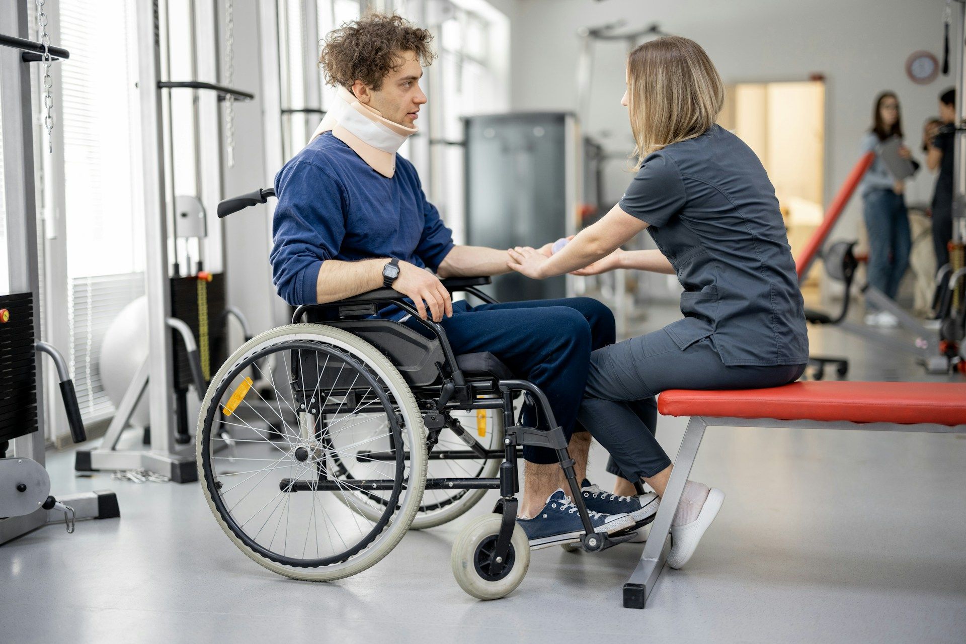 Physical therapist assisting a wheelchair user with arm exercises in a bright rehabilitation gym