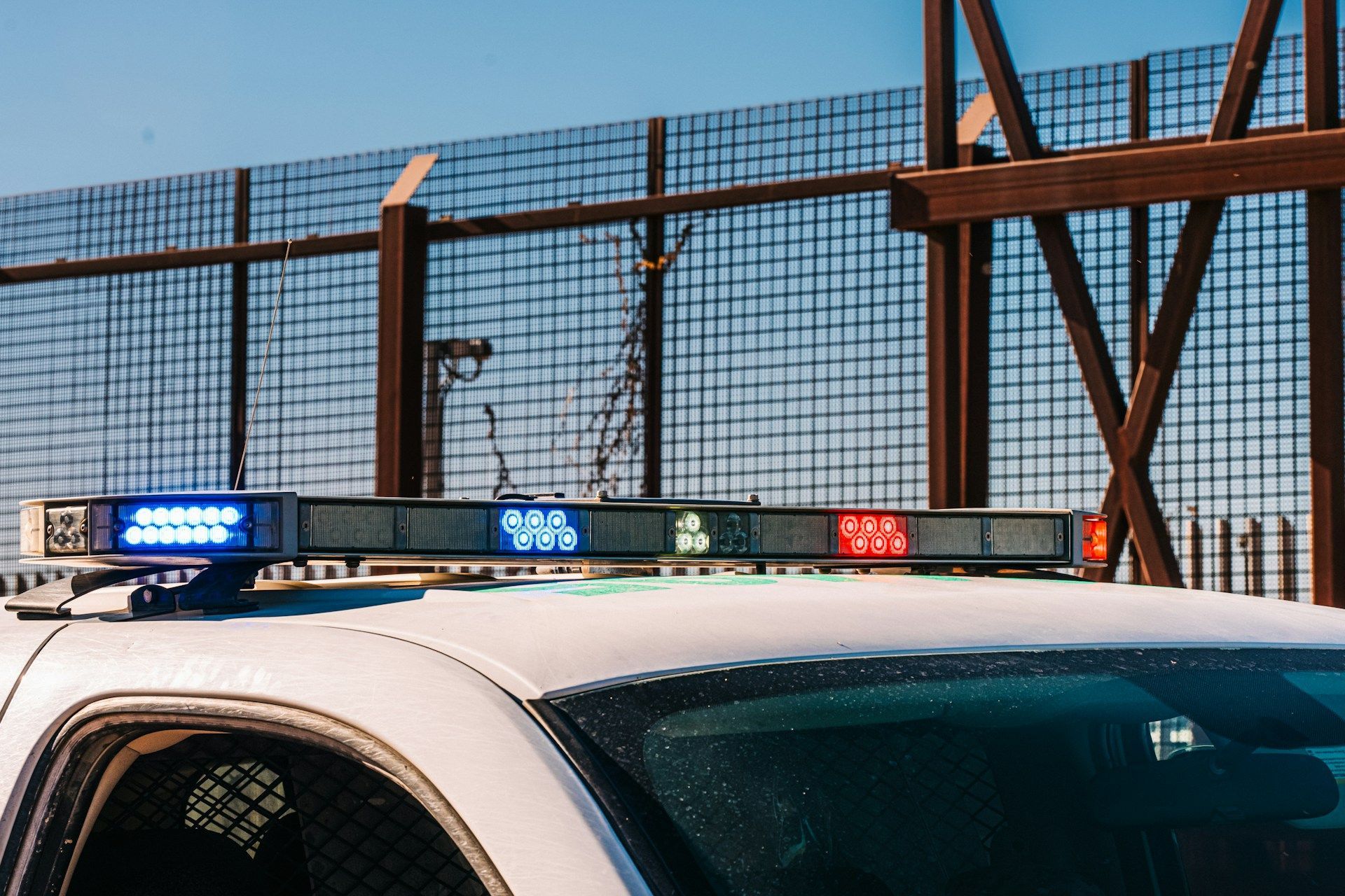 Police car with flashing blue and red lights near a metal fence at dusk