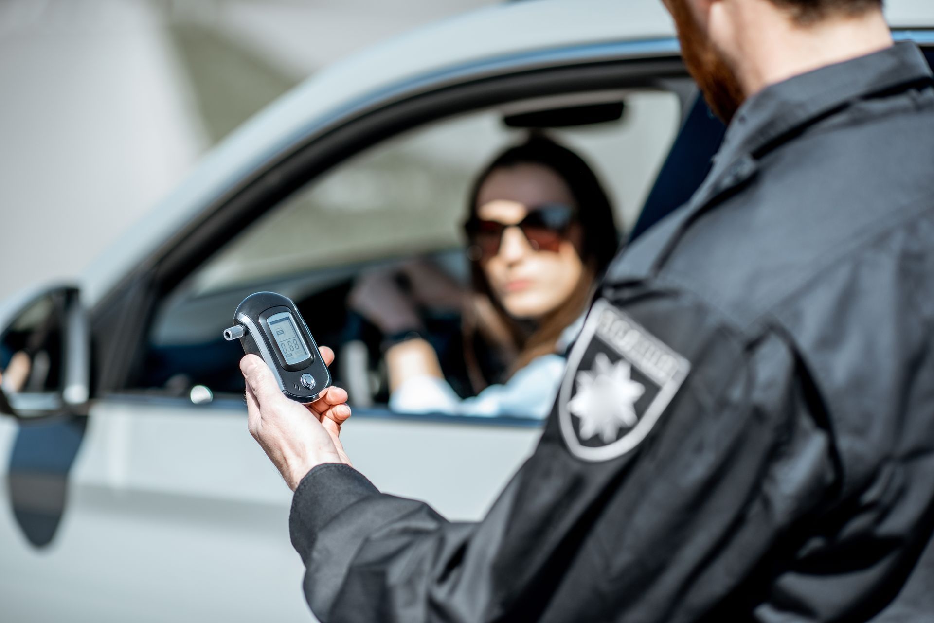 Police officer using a radar gun beside a car with a driver inside