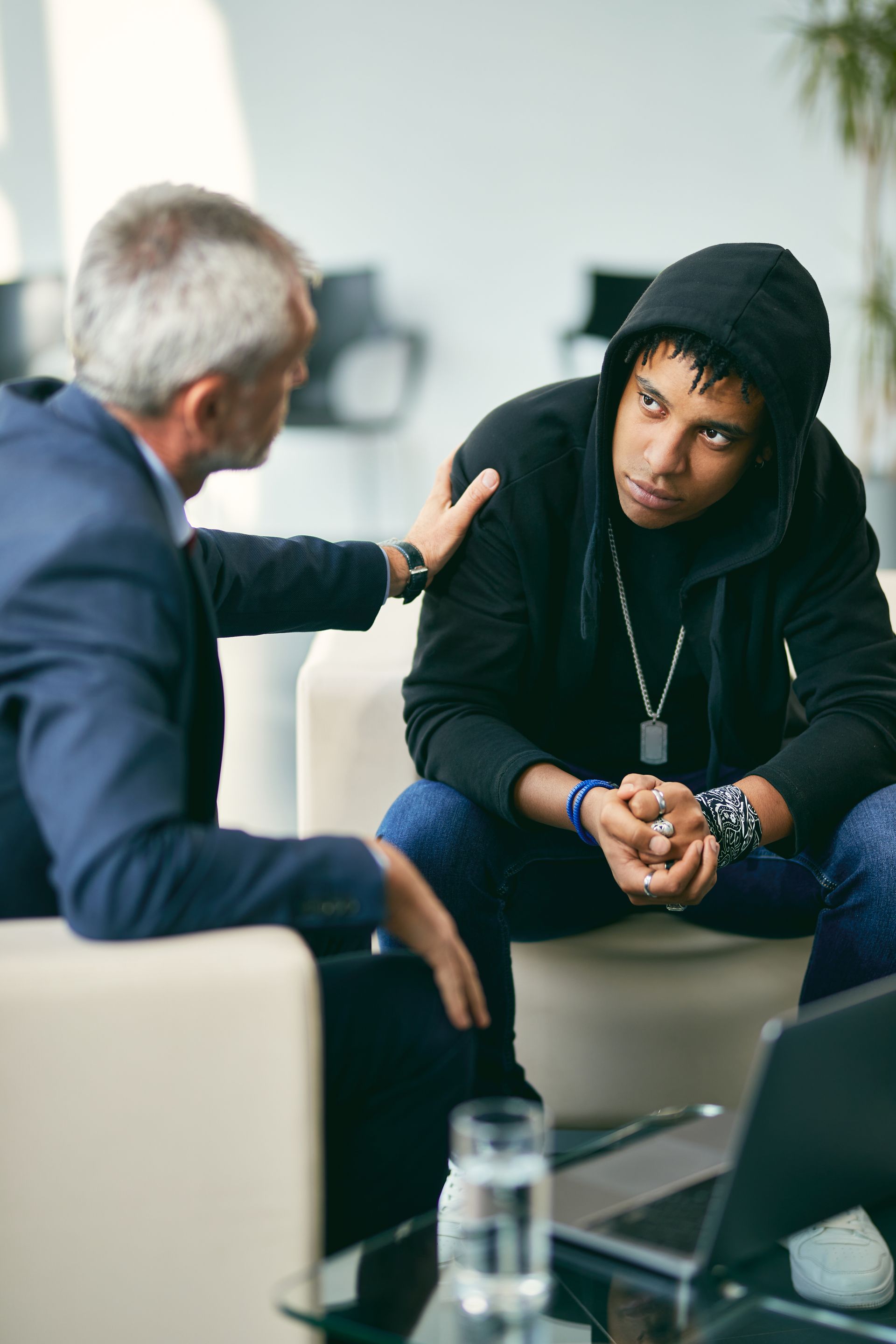 Two people in a modern office, one leaning in to comfort the other during a serious conversation