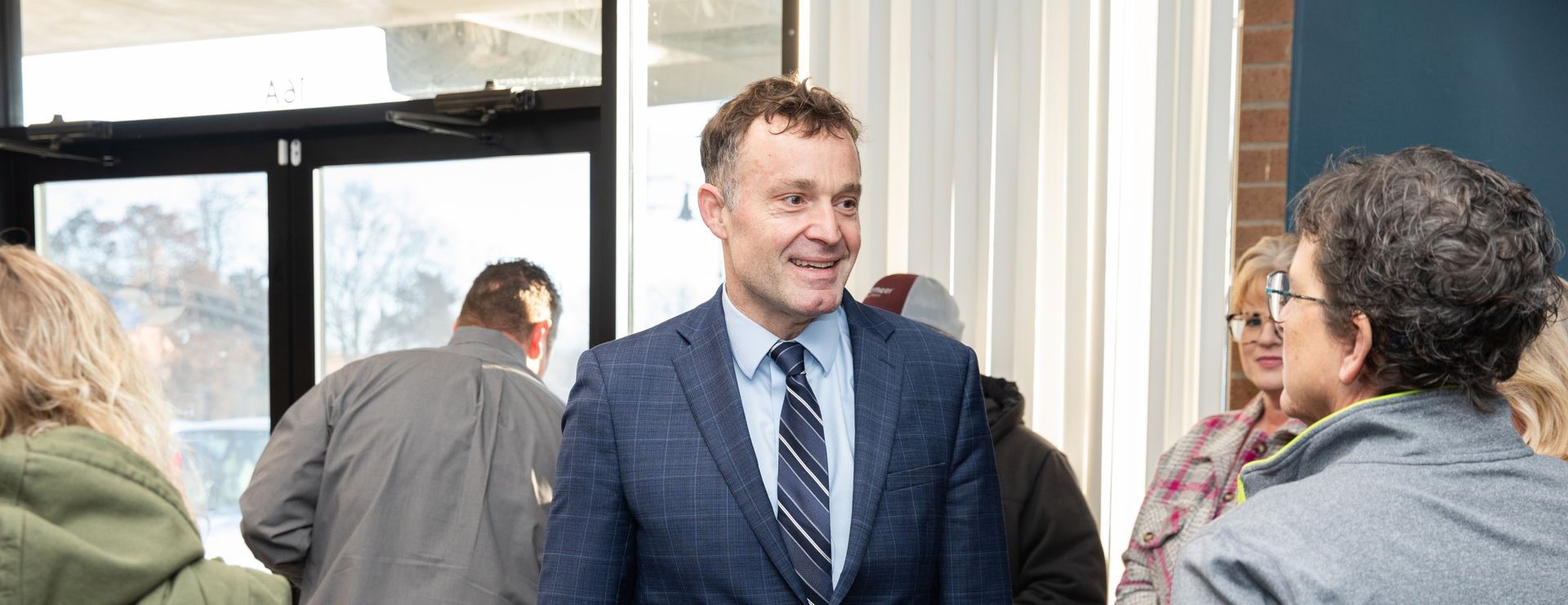 People talking in a bright office lobby, with a smiling man in a blue suit at center.