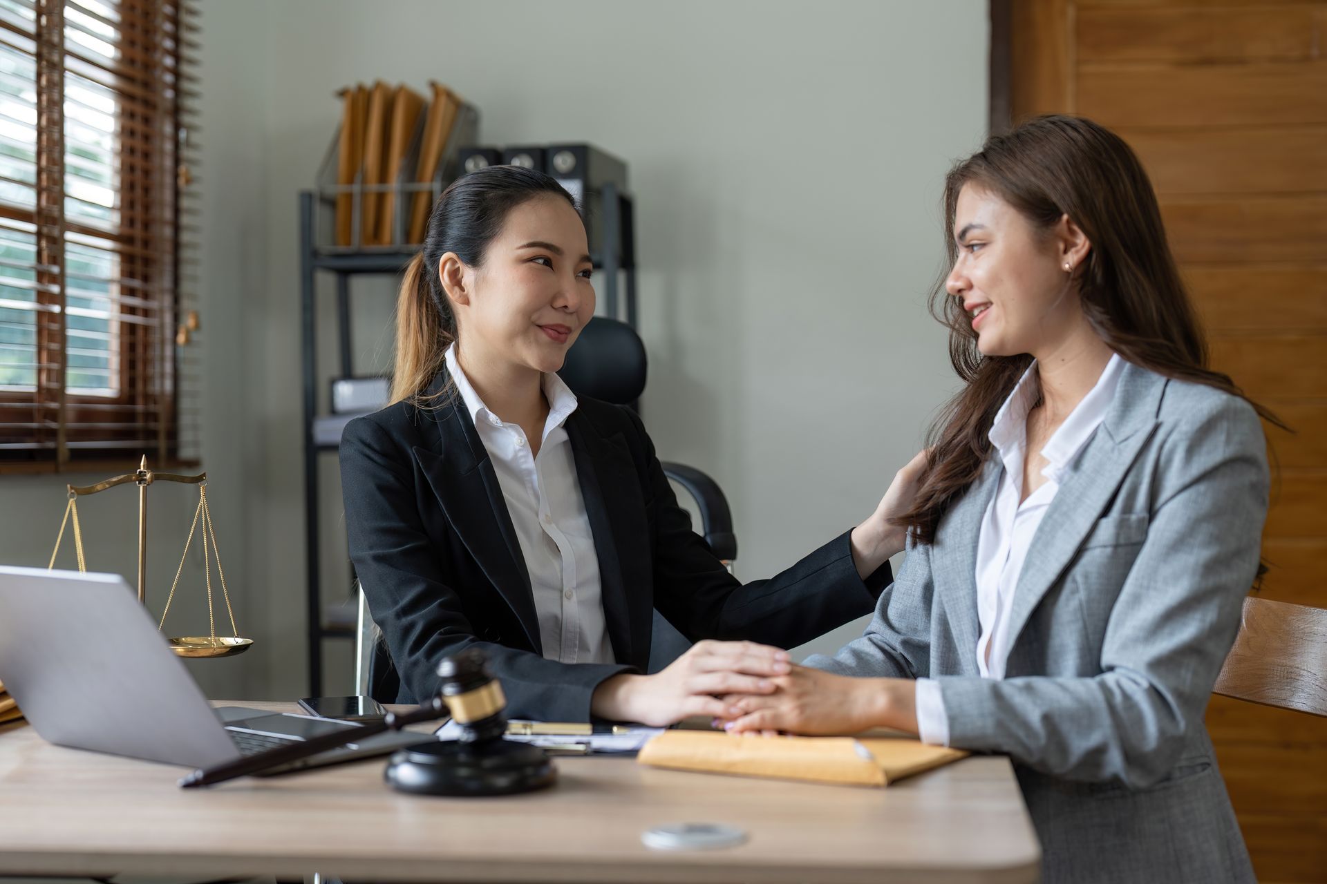 Two professionals in a meeting, one comforting the other at a desk in an office.