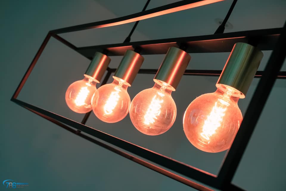 Four glowing Edison-style bulbs in a black, geometric light fixture.